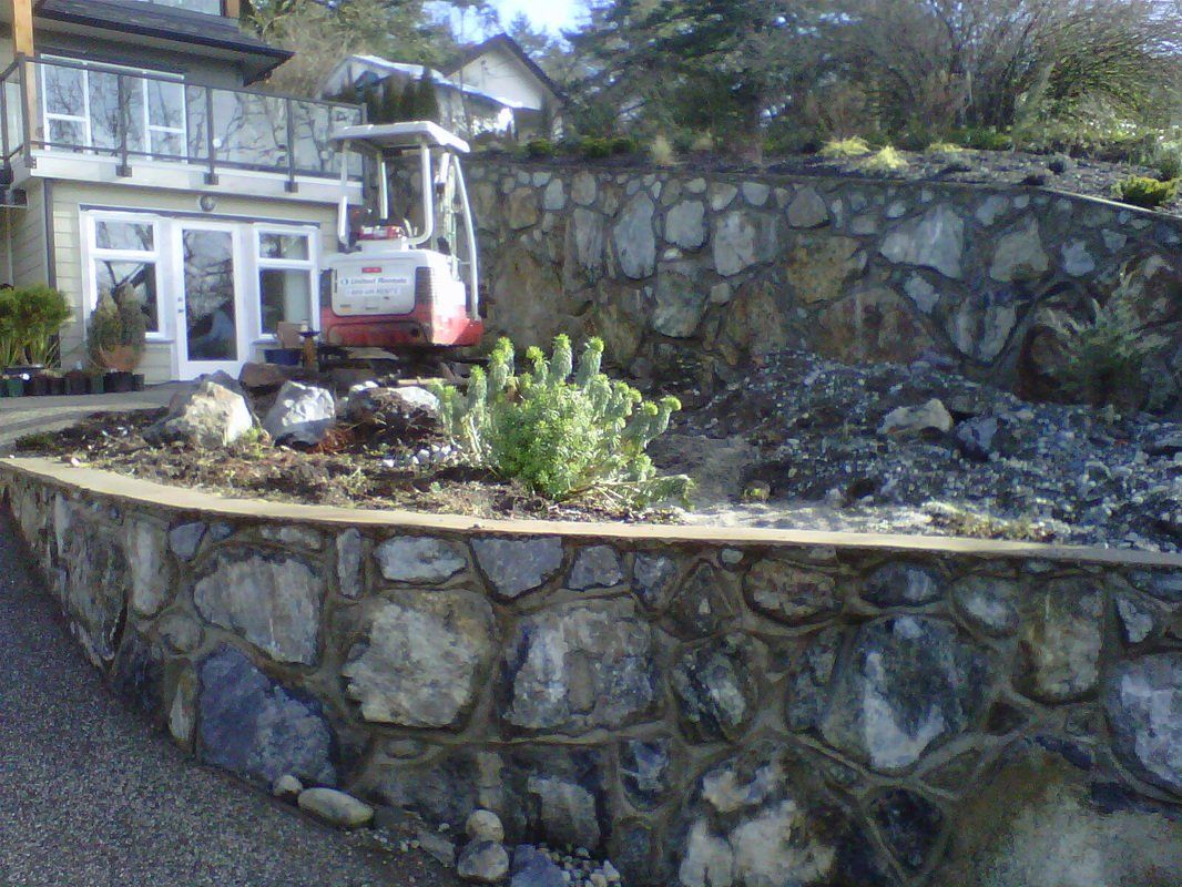 Residential front yard retaining wall made of natural stone and cement Two retaining walls in front of driveway with residential home in the background