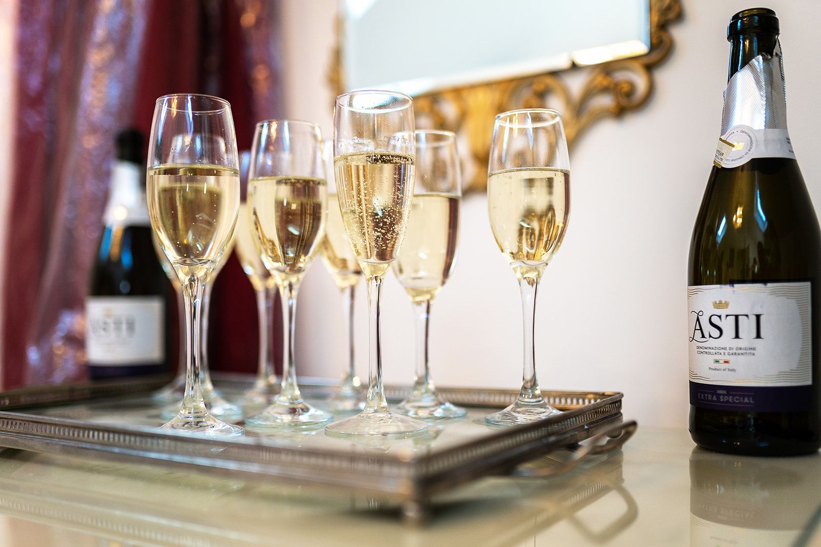 A bottle of asti is next to a tray of champagne glasses.