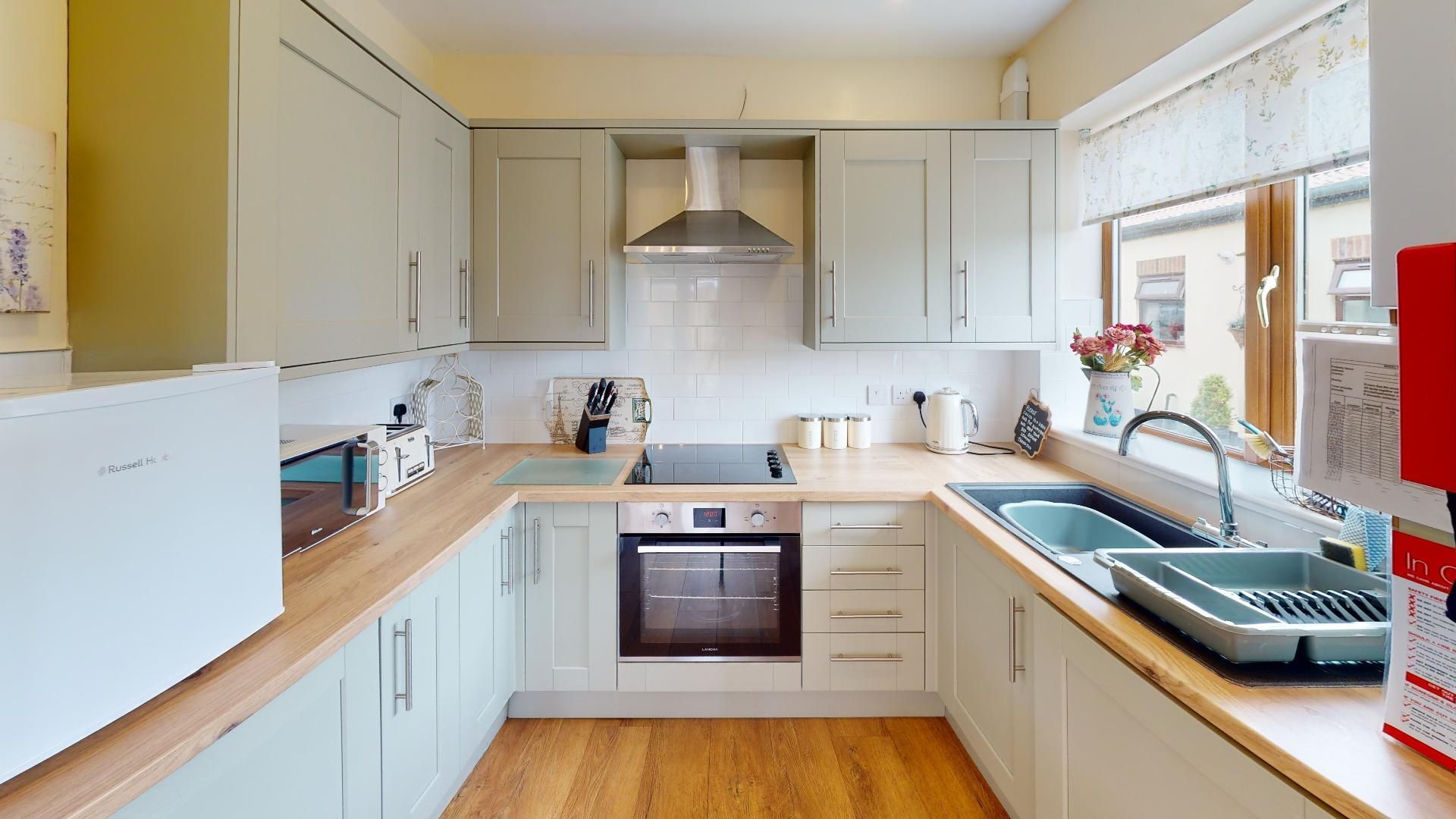 A kitchen with white cabinets , a stove , a sink , and a window.