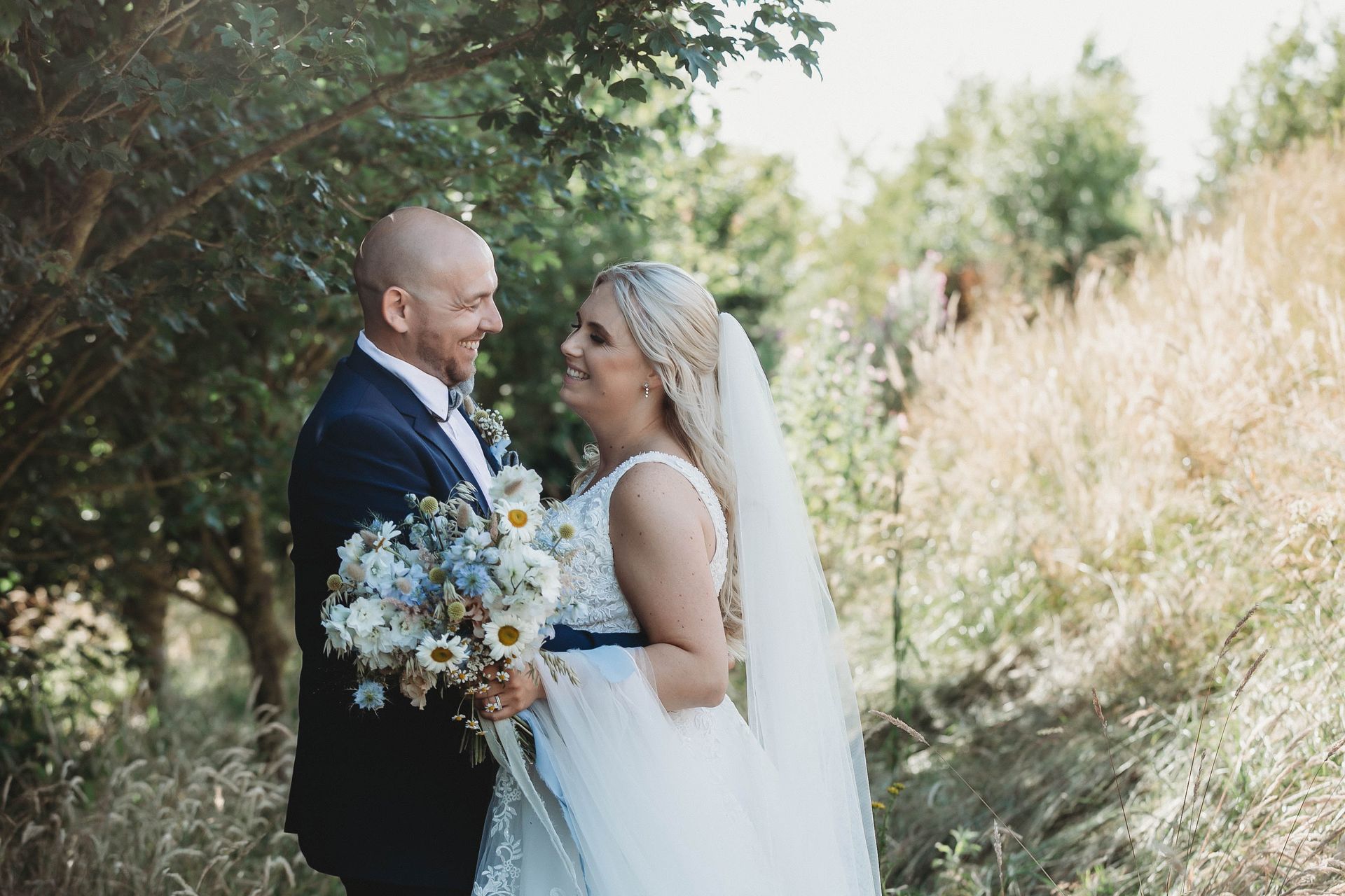 A bride and groom are standing in a field looking at each other.
