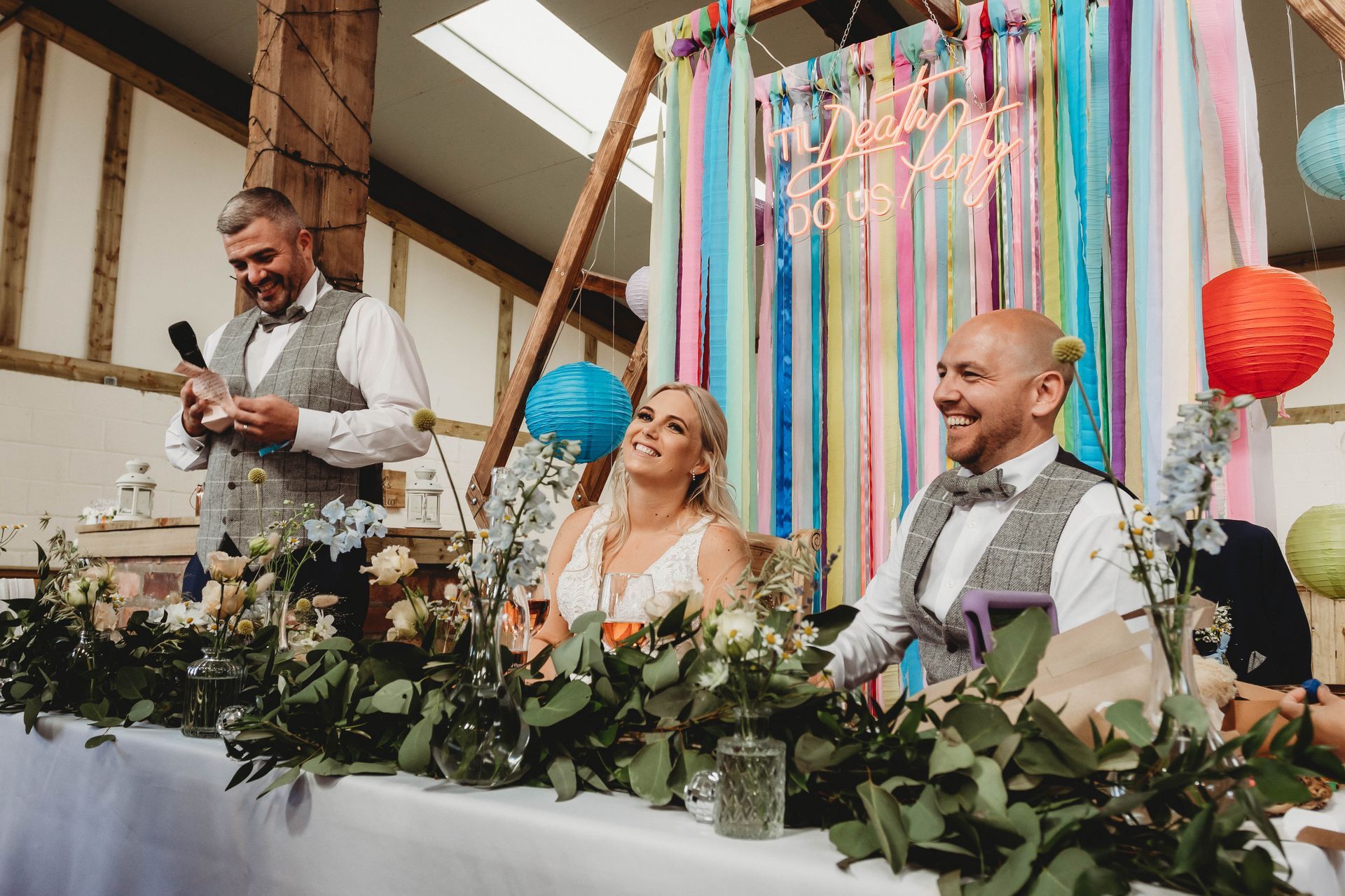 A bride and groom are sitting at a long table at a wedding reception.