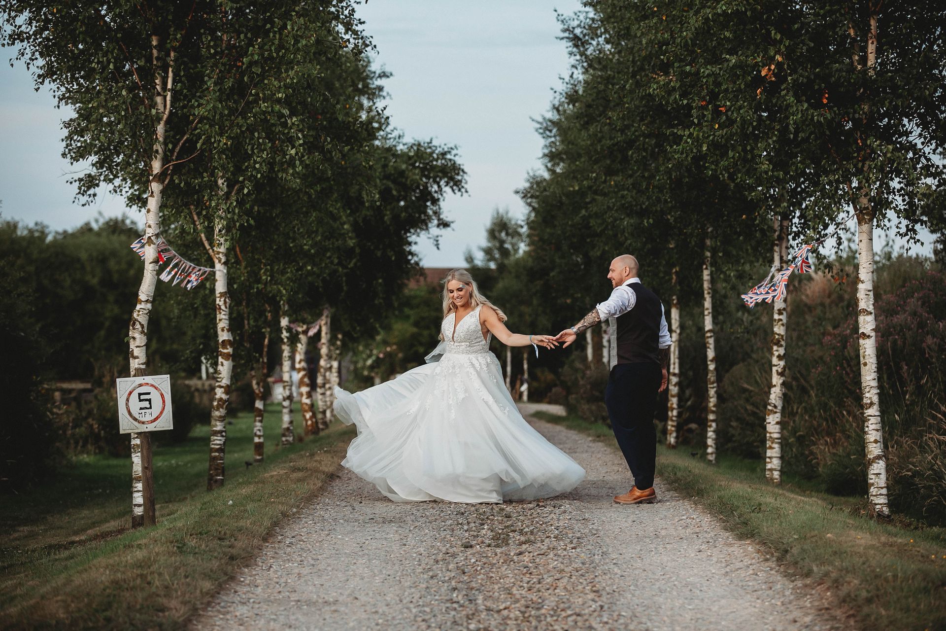 A bride and groom are walking down a dirt road holding hands.