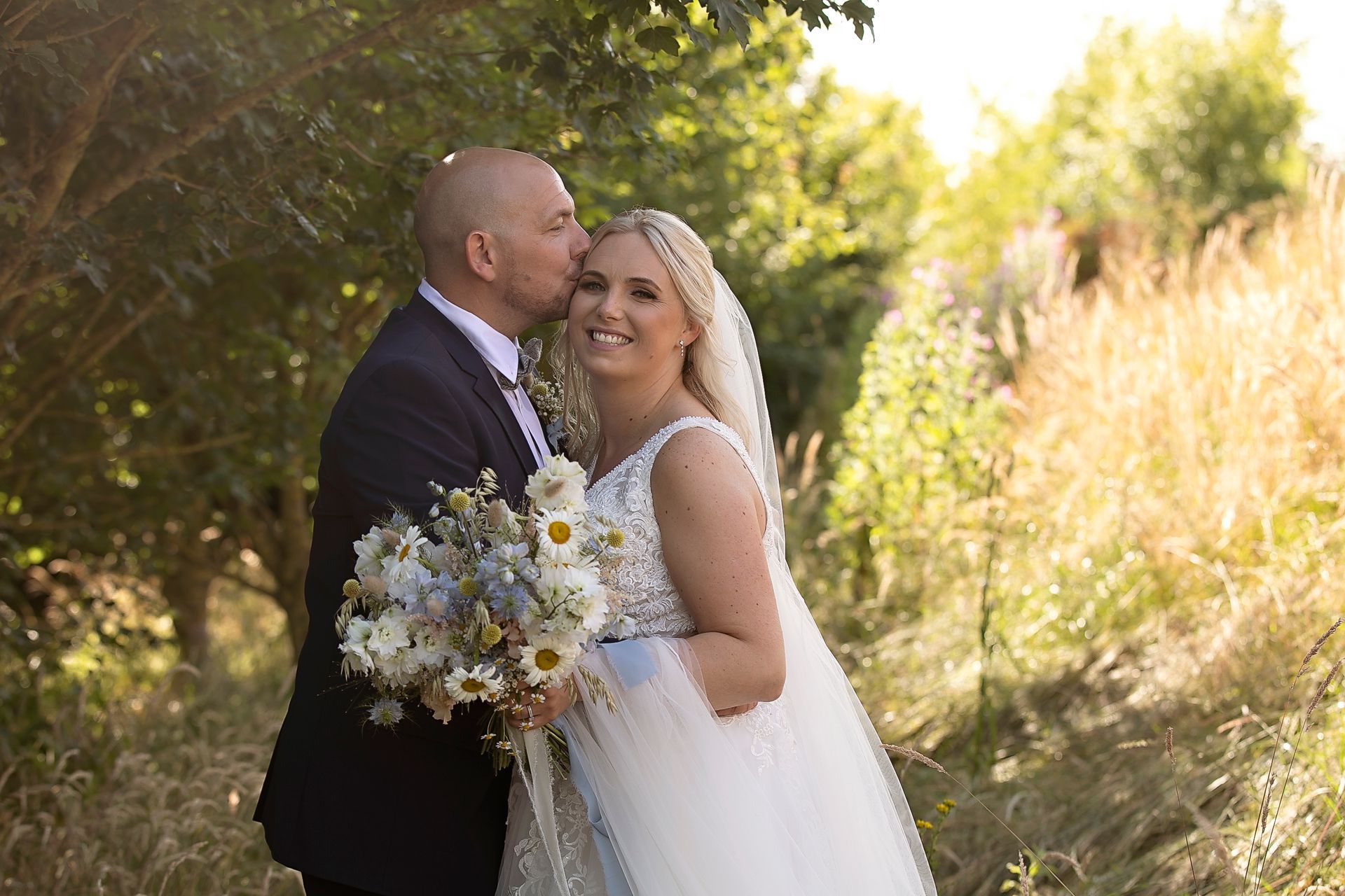 A bride and groom are kissing in a field.