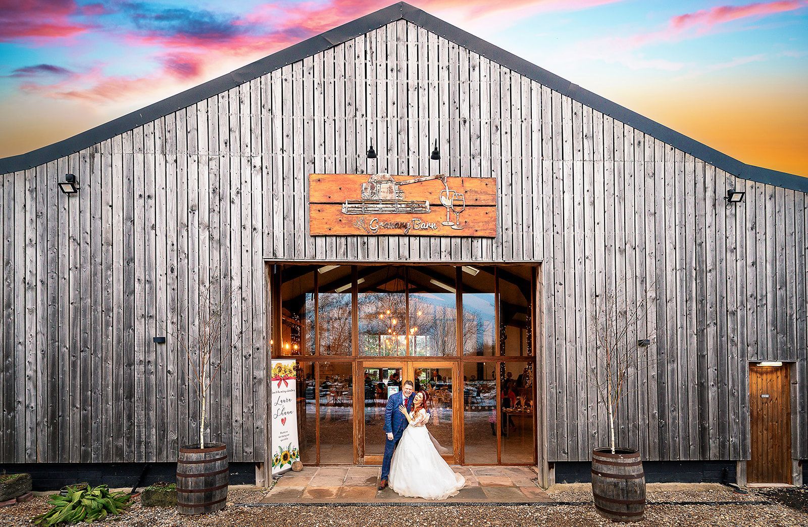 A bride and groom are standing in front of a wooden barn.