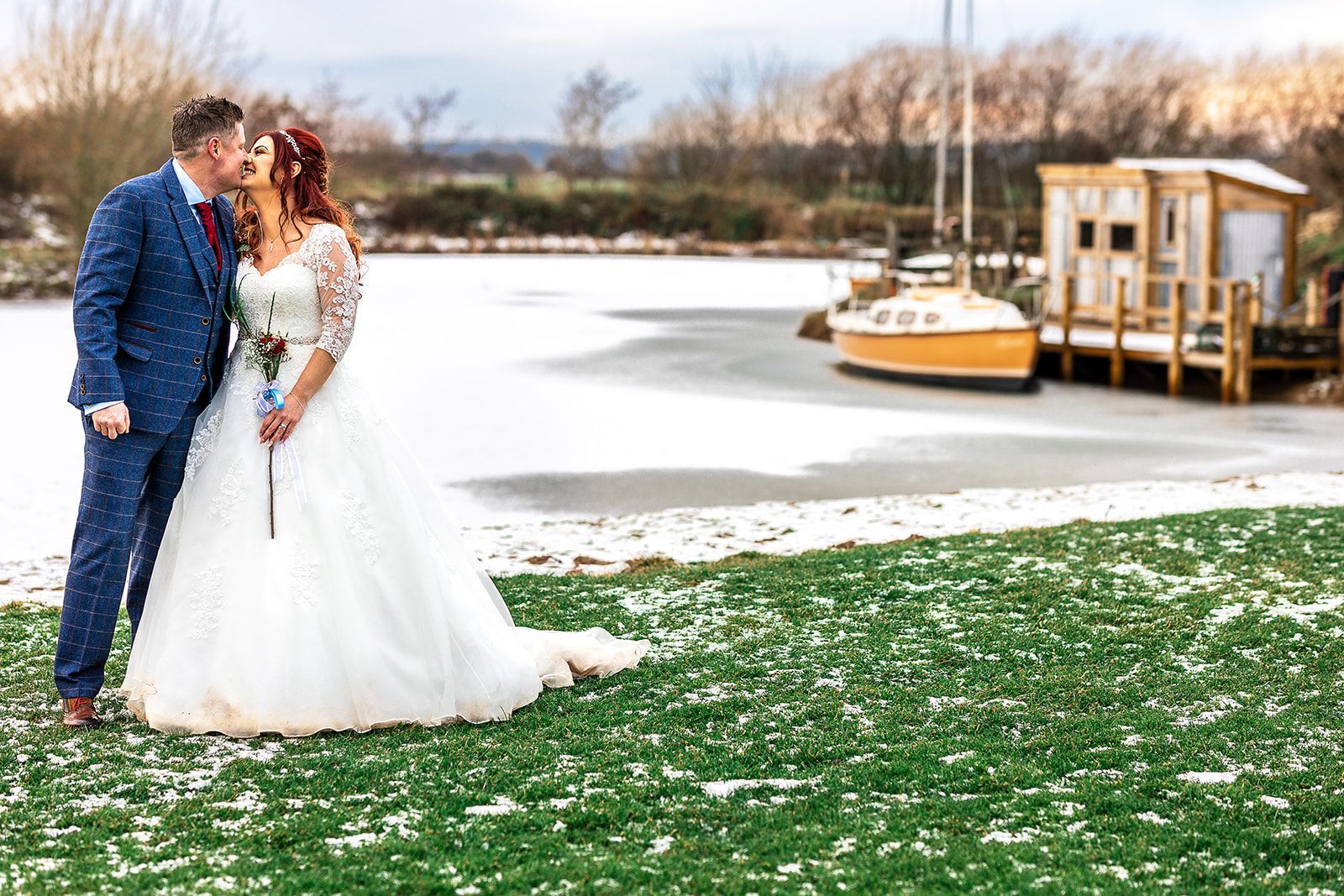 A bride and groom are kissing in front of a frozen lake.