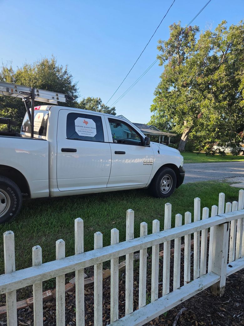 White pickup truck parked beside a white picket fence on a sunny suburban street.