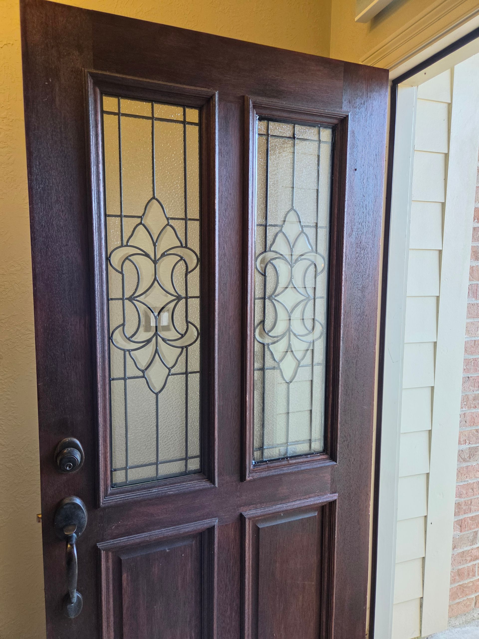 Front door with dark wood and decorative glass panels, viewed from outside a yellow exterior wall.