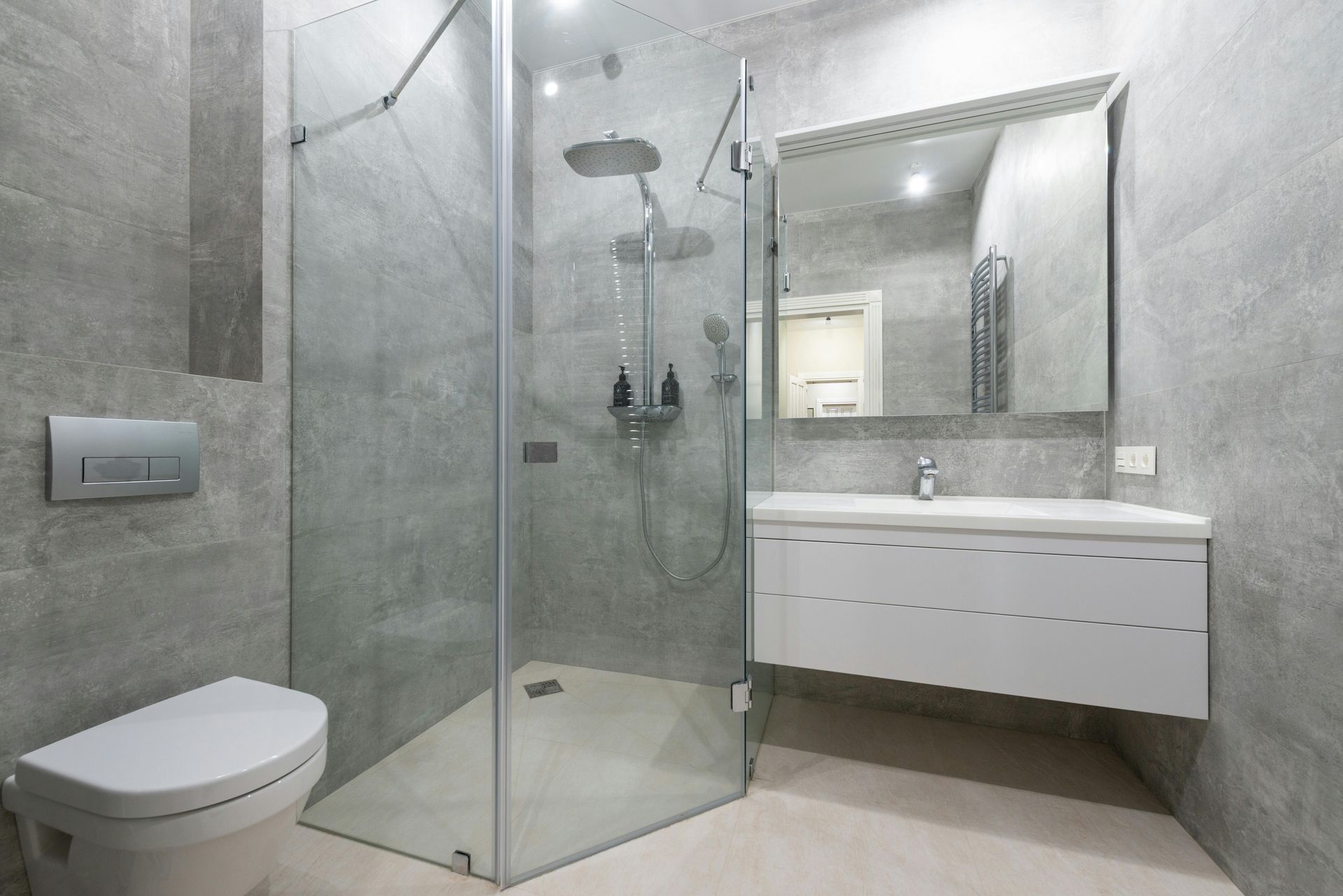 Modern gray bathroom with glass shower, floating vanity, and toilet.