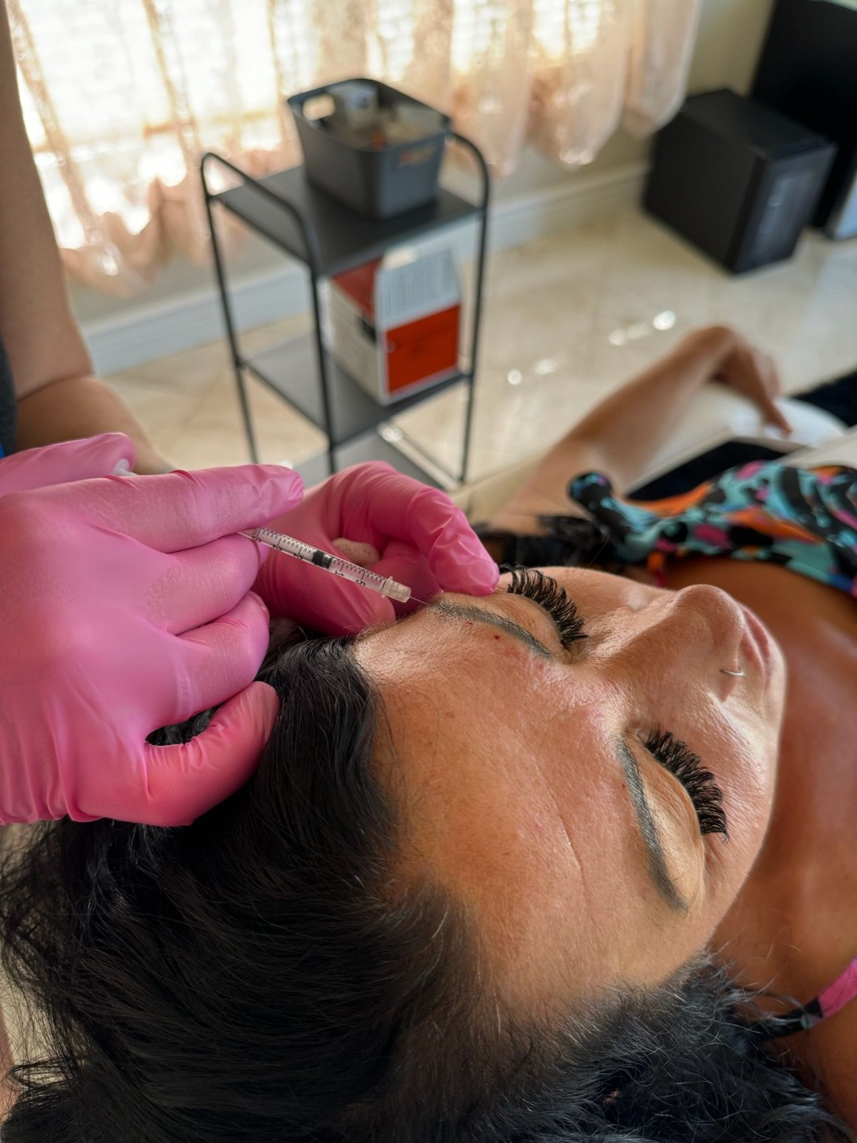 Jordana's pink gloved hands injecting botox into a young womans face  