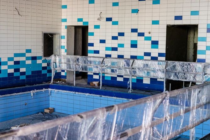 Indoor tiled pool under renovation, with blue-tiled walls, plastic sheeting, and construction materials.