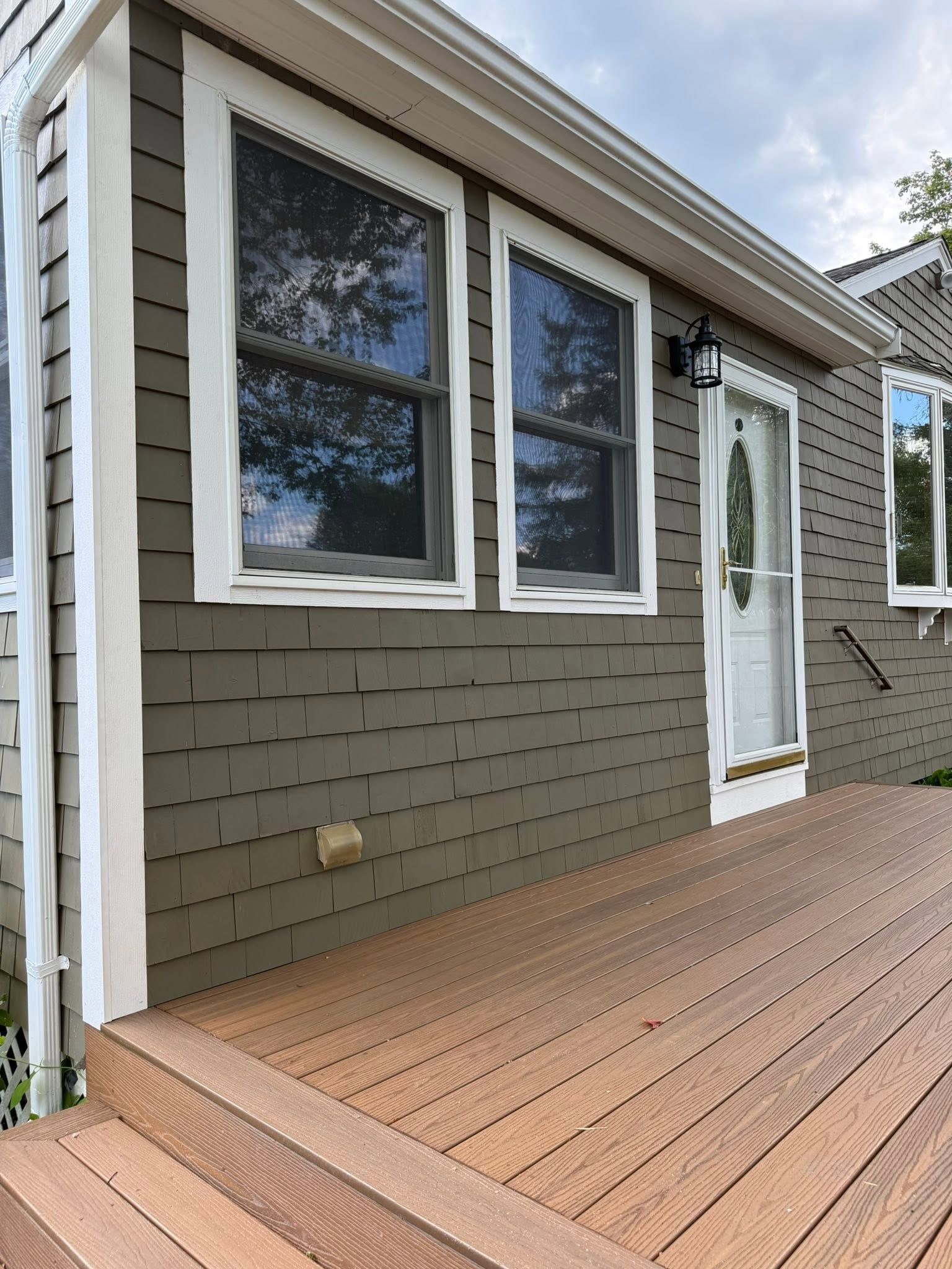 Exterior of a house with gray siding, white-trimmed windows, and a wooden deck and steps.