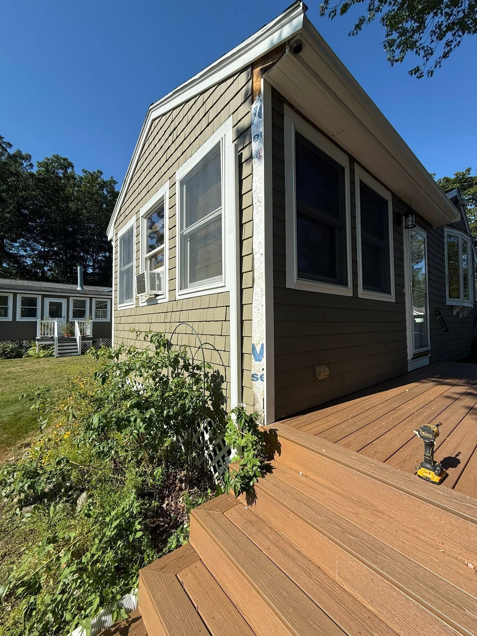 Small beige house exterior with wooden deck steps and windows in bright sunlight