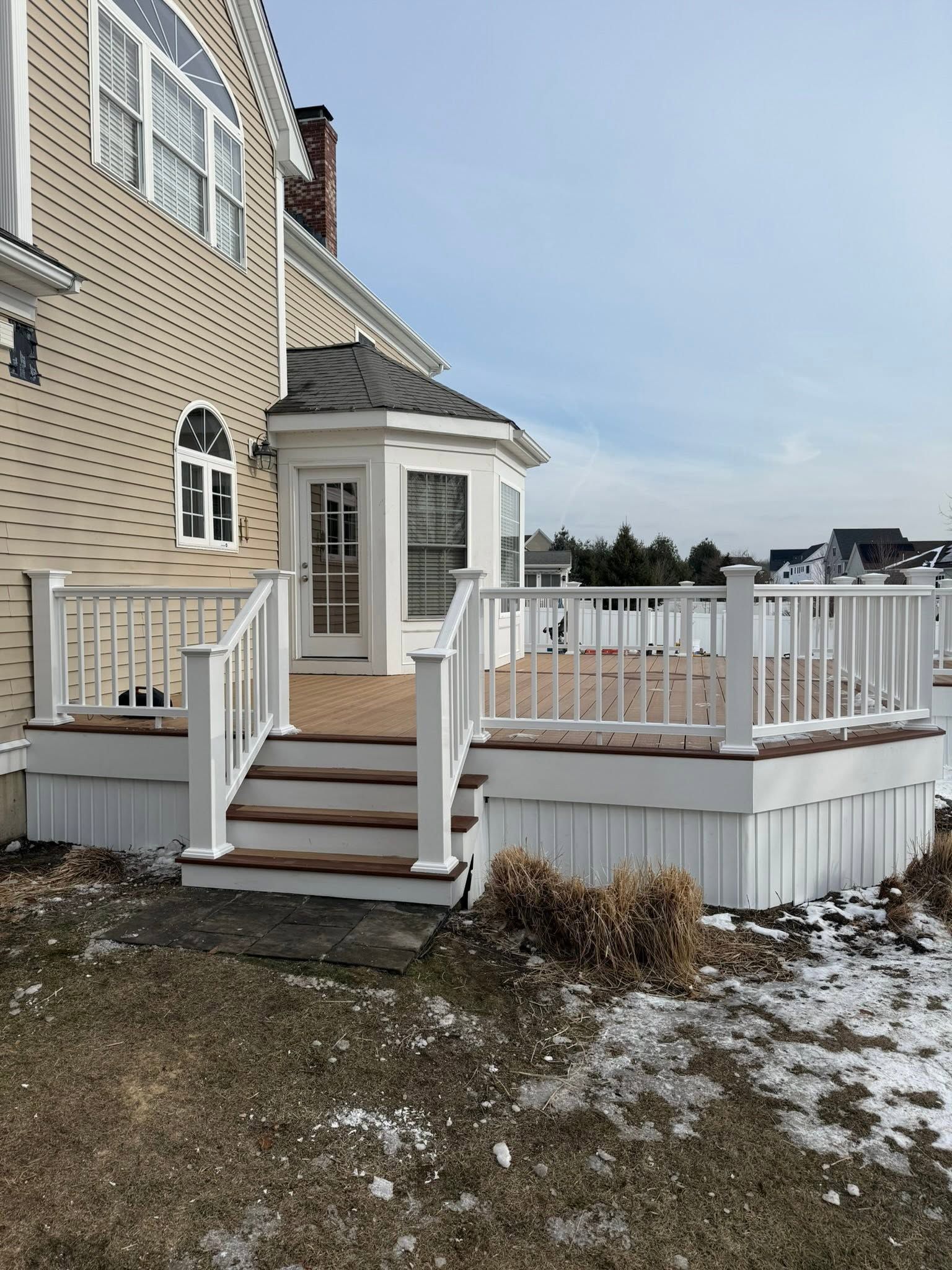 Side entrance porch with white railings and steps on a beige house in a snowy yard.