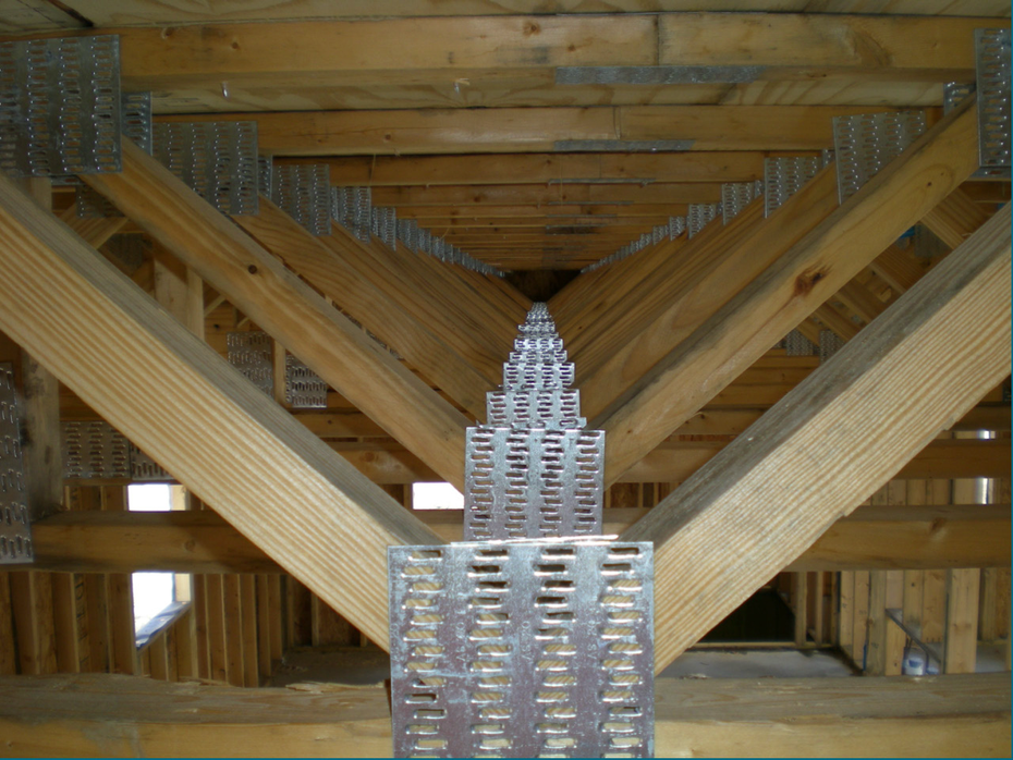 Steel building framework under construction on a paved site under a clear blue sky