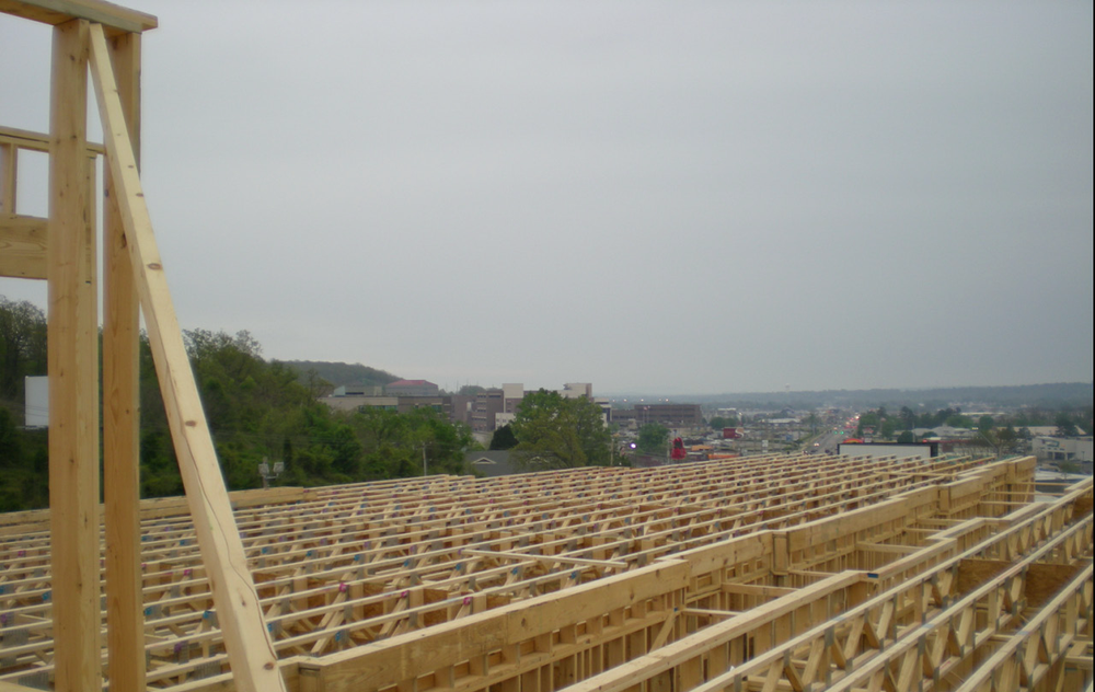 Yellow roof trusses under construction against a cloudy sky, with a crane lifting a beam