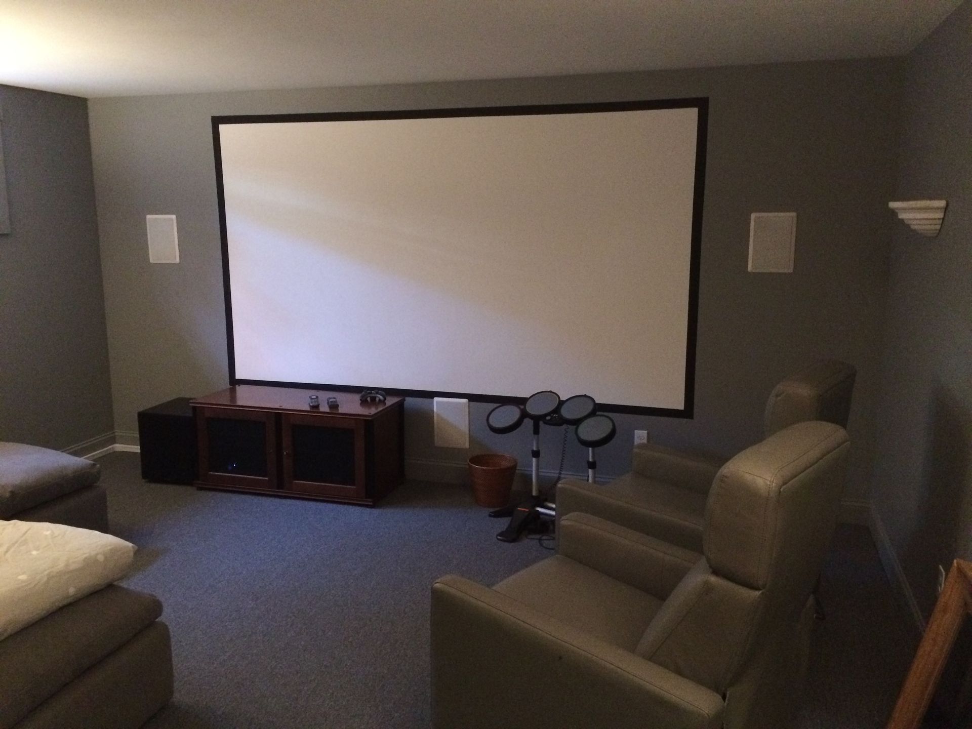 A home theater featuring a large projection screen on a gray wall, a wooden media console, and gray reclining armchairs.
