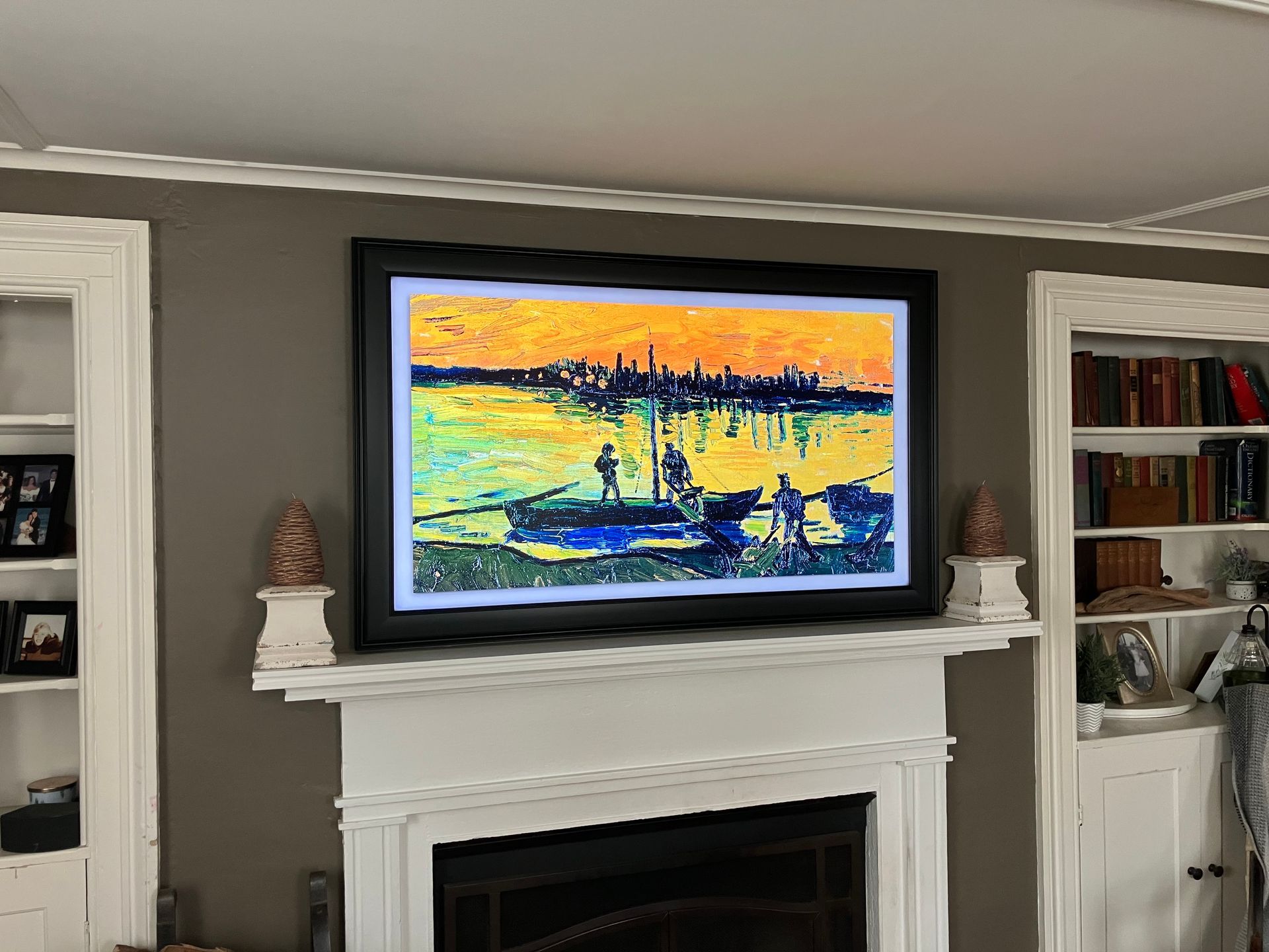 A television displaying a vibrant impressionist painting of a boat on water, mounted above a white fireplace in a room.