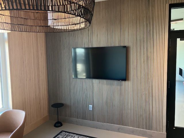 A flat-screen TV mounted on a light wood slat wall, next to a small side table and a partial view of a chair.