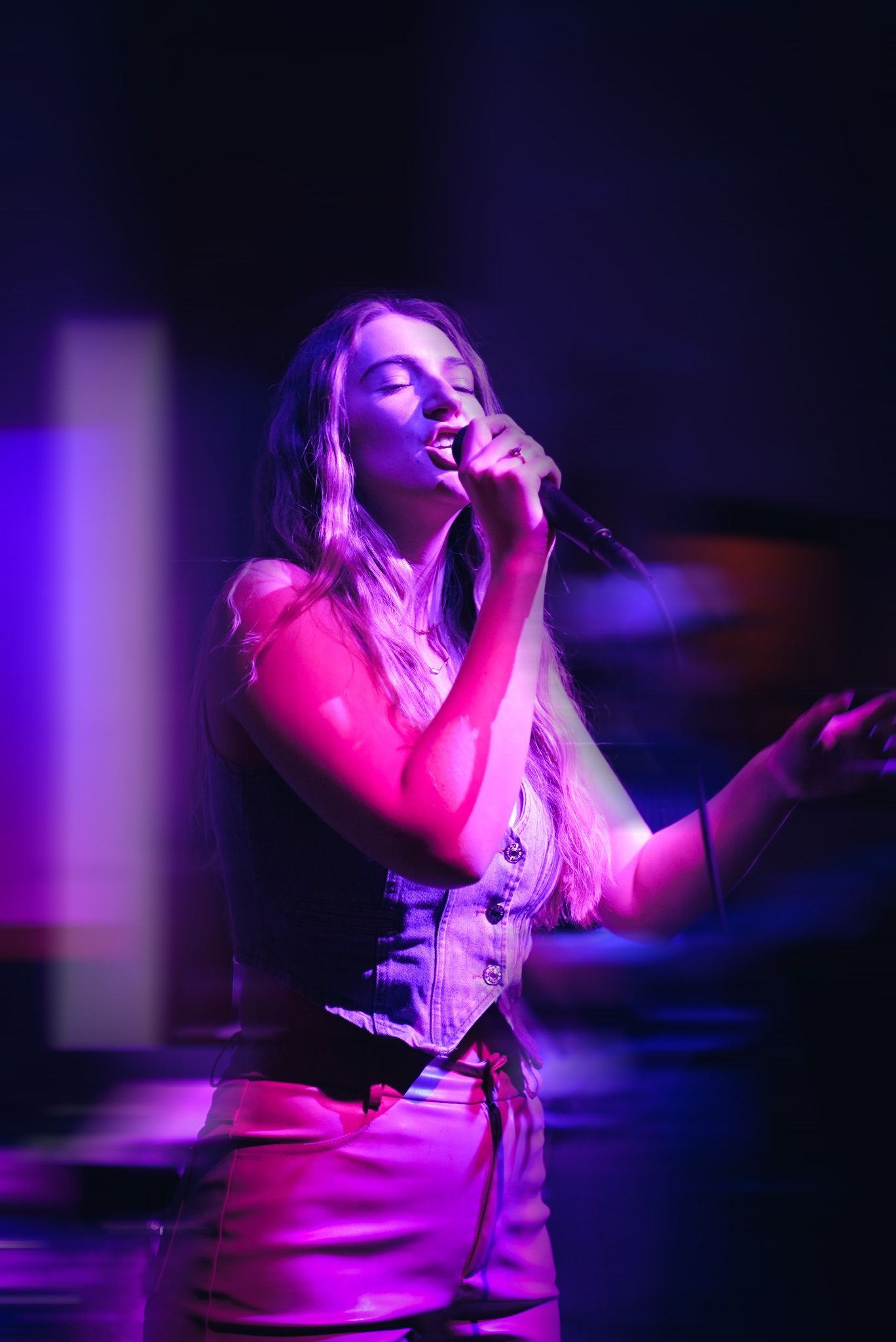 A girl sings at a live concert in a blue and pink lit room.