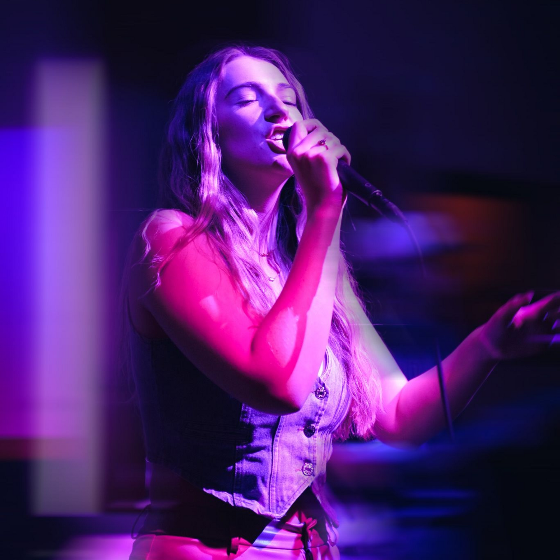 A girl singing at a concert with blue and pink lighting.
