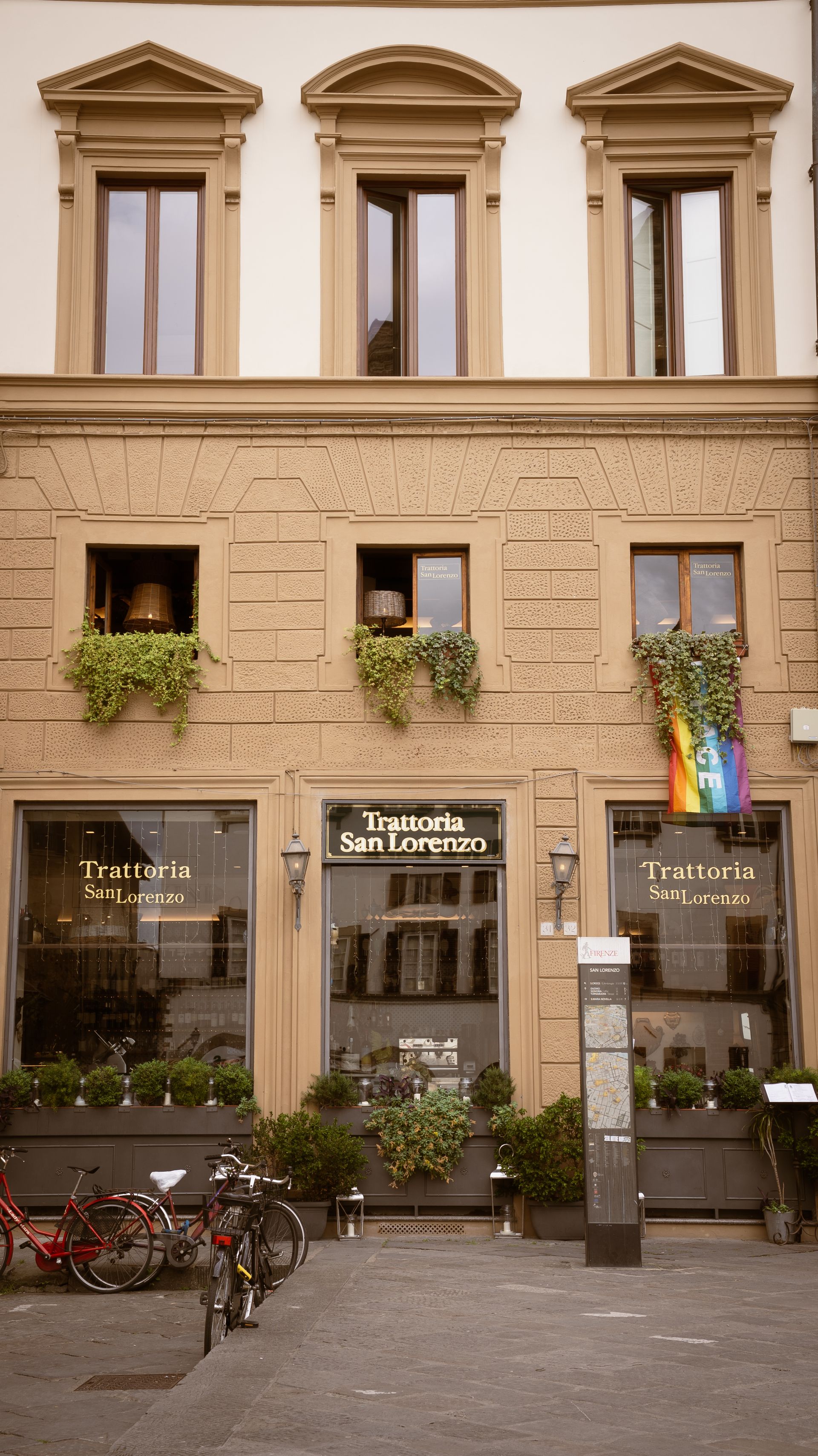 The front of a restaurant in Florence, Italy with a pride flag hanging in the window.