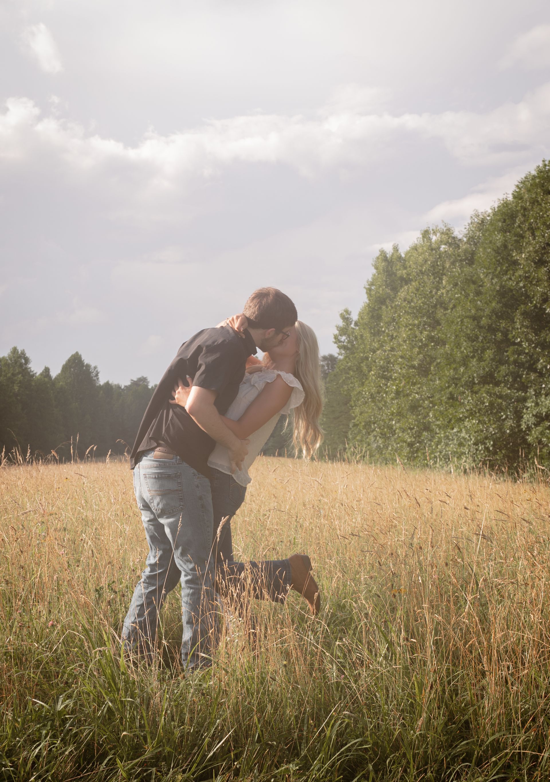 Wide shot of a couple kissing in a field at sunset for a couple photo shoot.