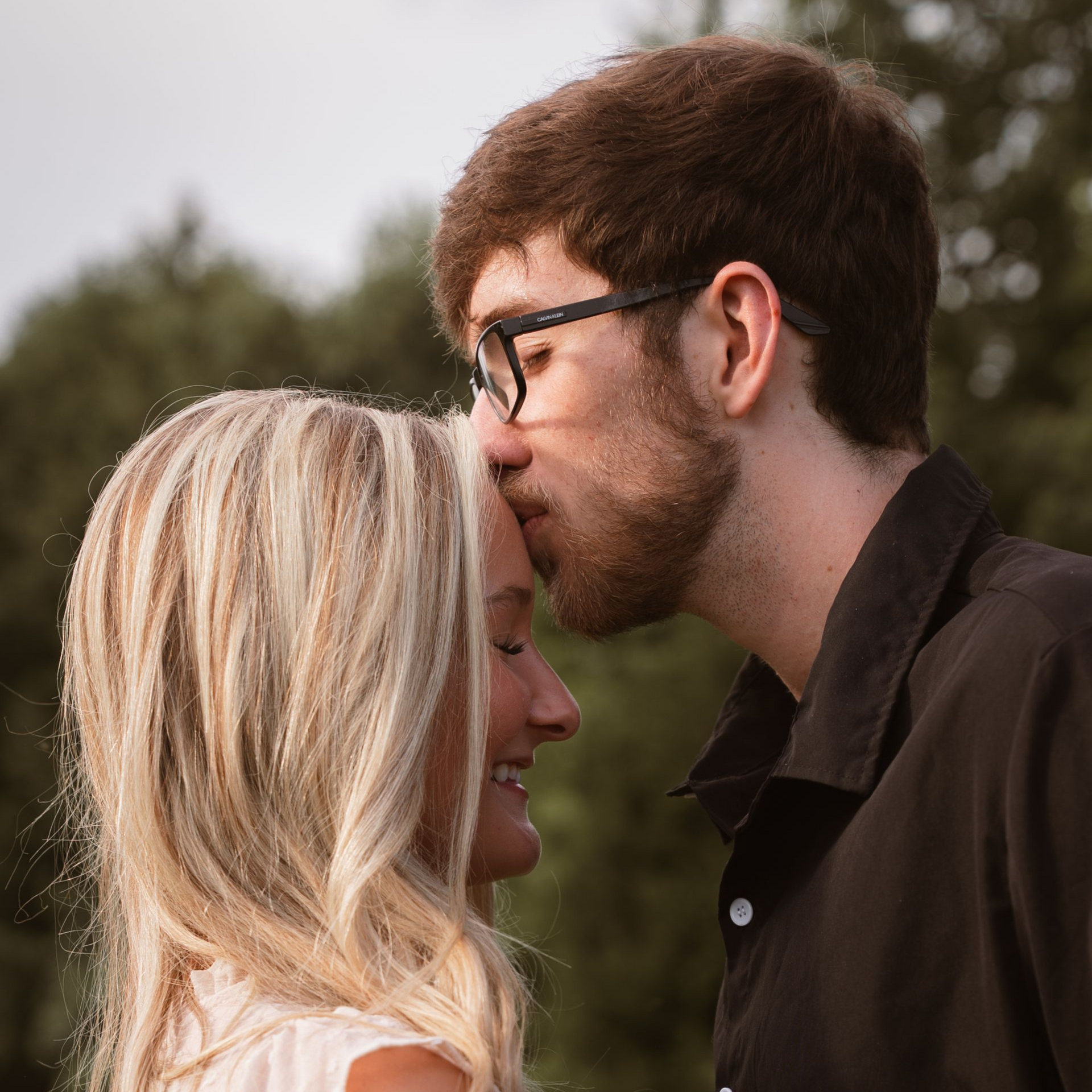 A man kisses his girlfriend on the forehead as she smiles for couple photos.