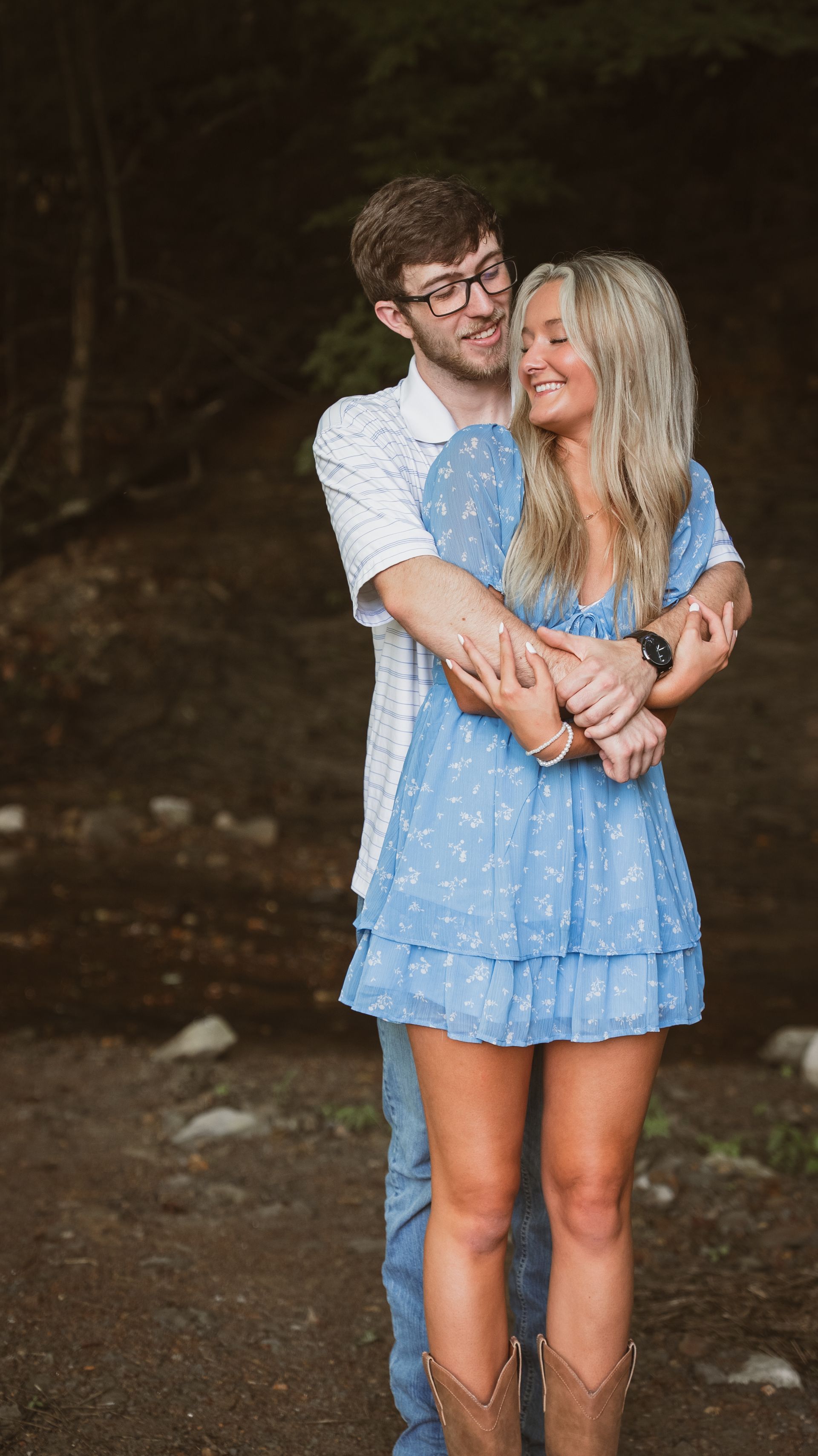 Wide shot of a couple standing on a creek bed. The man has his arms wrapped around his girlfriend.