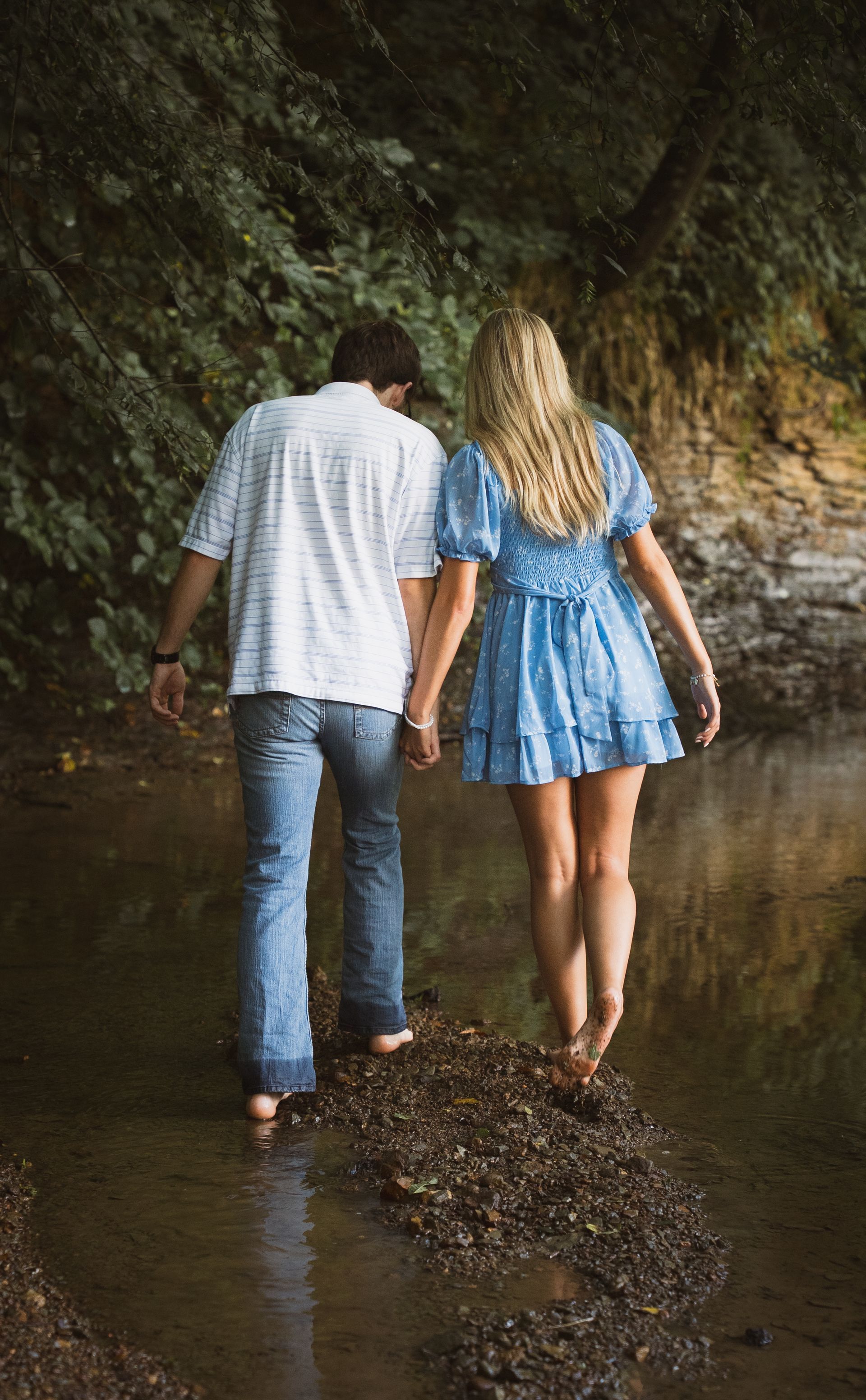 A man and a woman walk through a shallow creek together, holding hands.