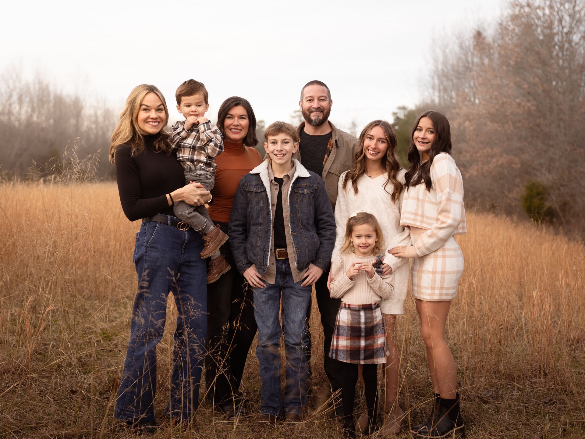 A family posing together for family photos in a field at sunset.