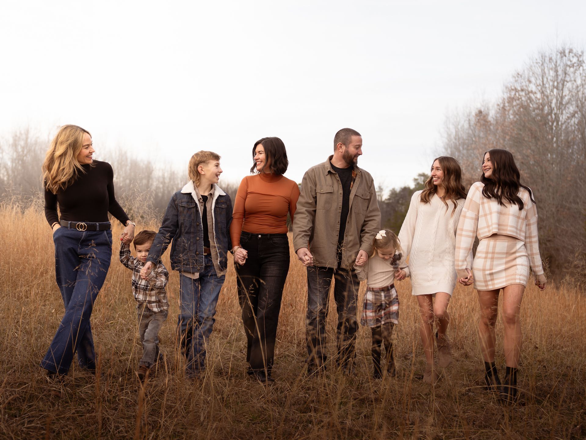 A family walking through a field at sunset holding hands and laughing with each other.