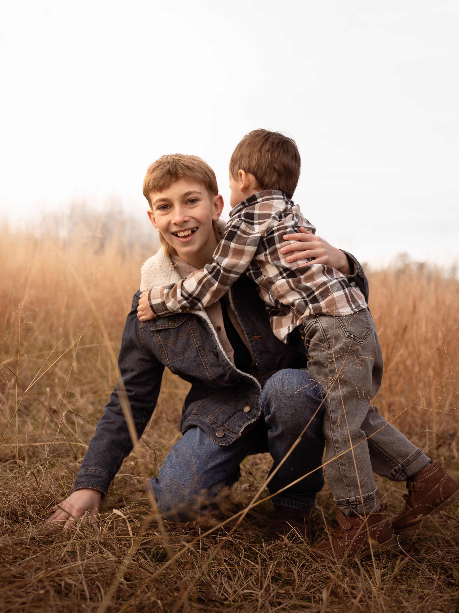 A young child tackles his older cousin in a field at sunset for family photos.