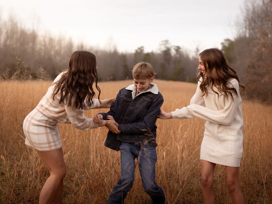 Three siblings playing together in a field at sunset.