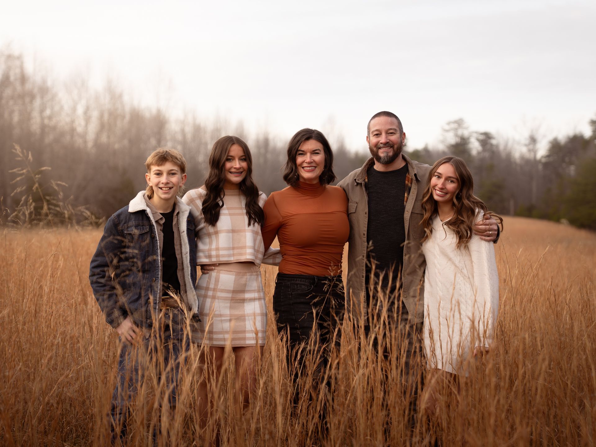 A family poses together for family photos in a field at sunset.