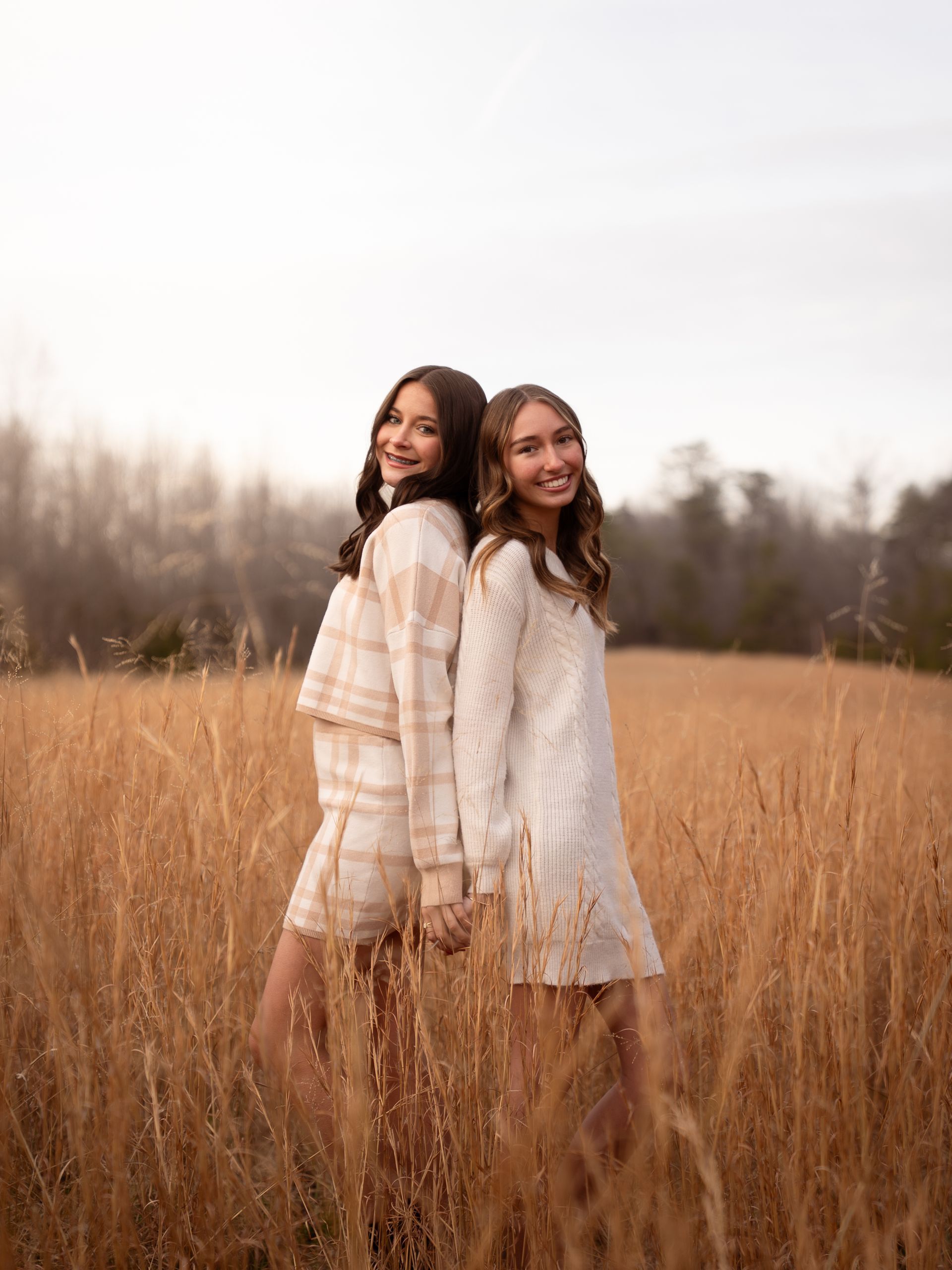 Two sisters posing together for family photos in a field at sunset.