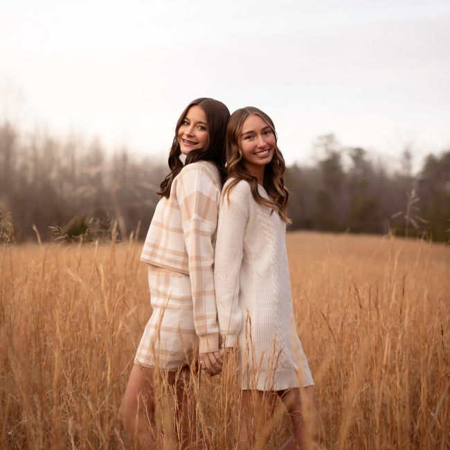 Two sisters posing for family photos in a field at sunset.