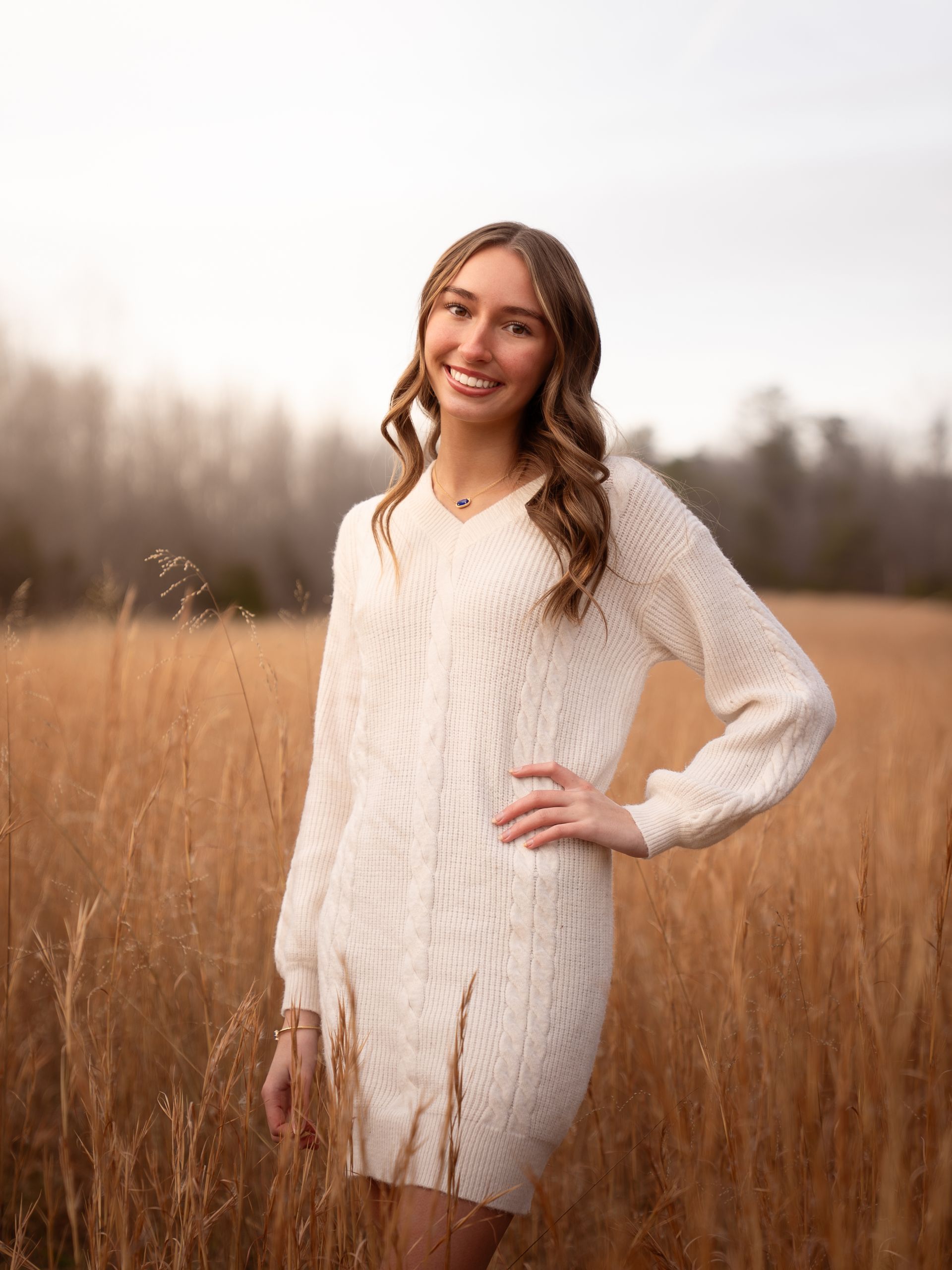 Girl standing in a field at sunset smiling at the camera for senior photos.