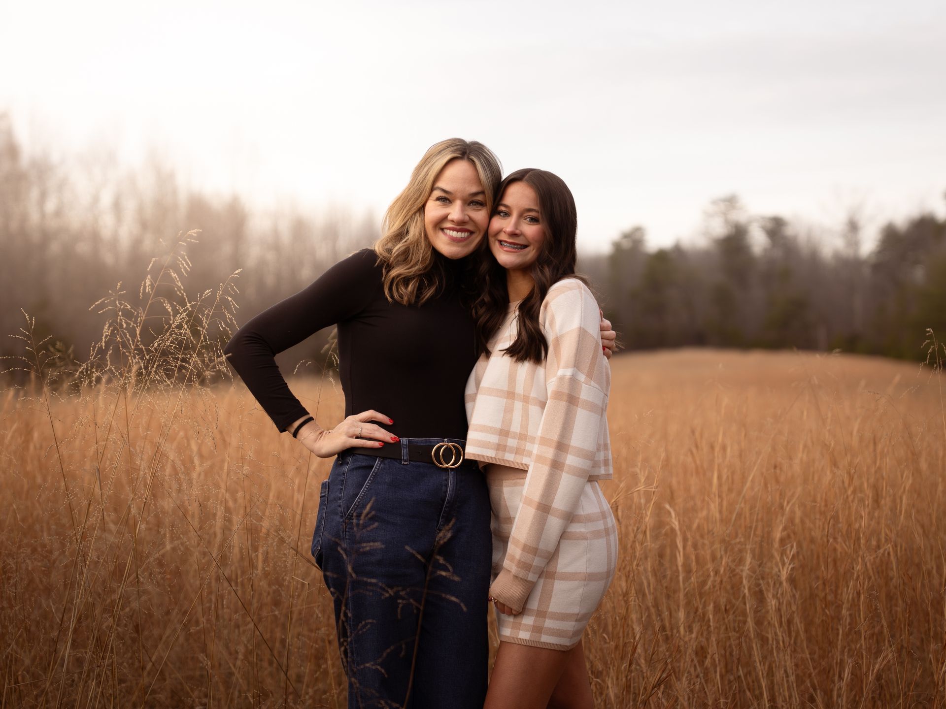 A girl and her aunt posing for family photos together in a field at sunset.