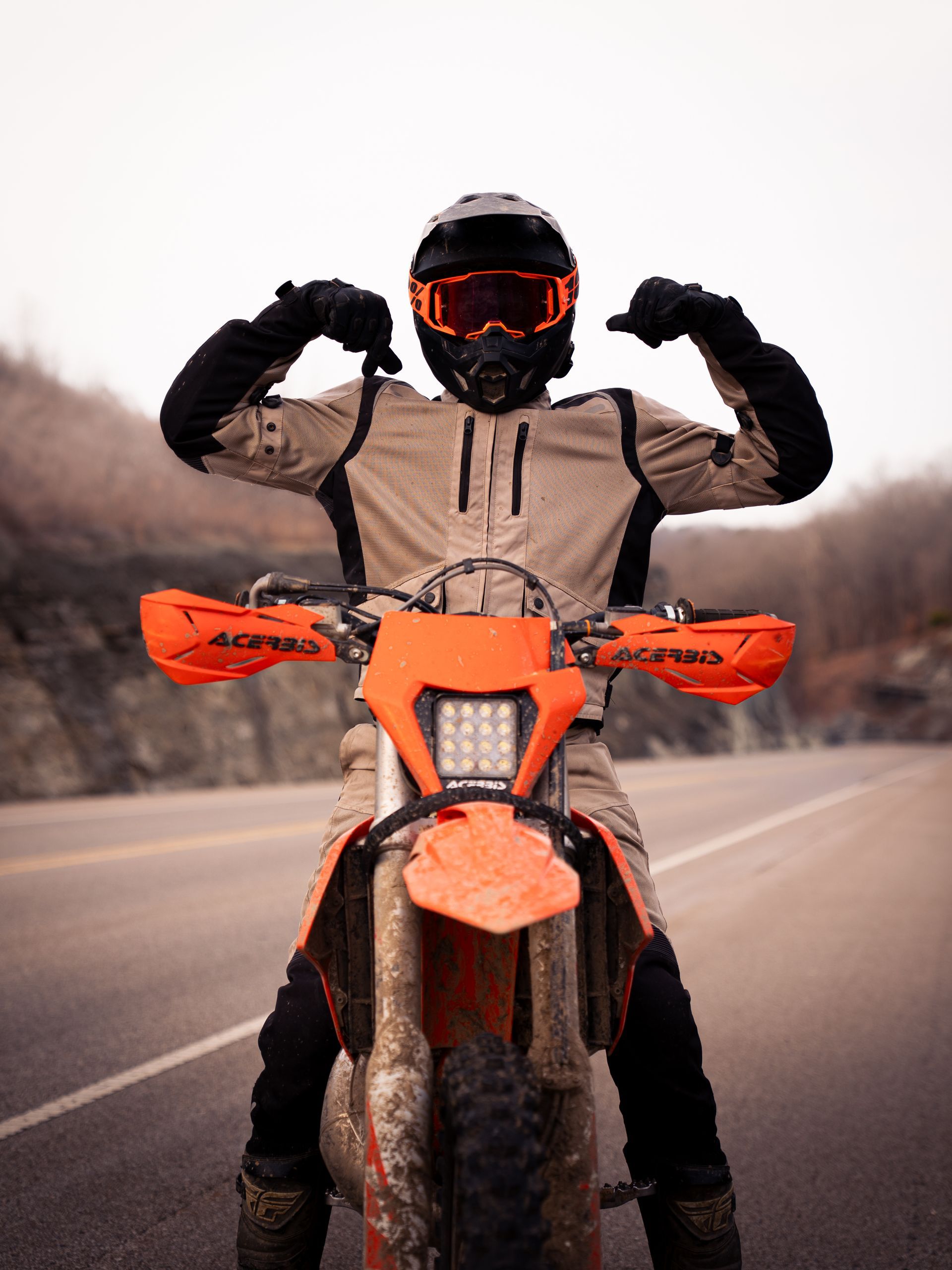 Boy sitting on a dirt bike on a mountain road, flexing his muscles.