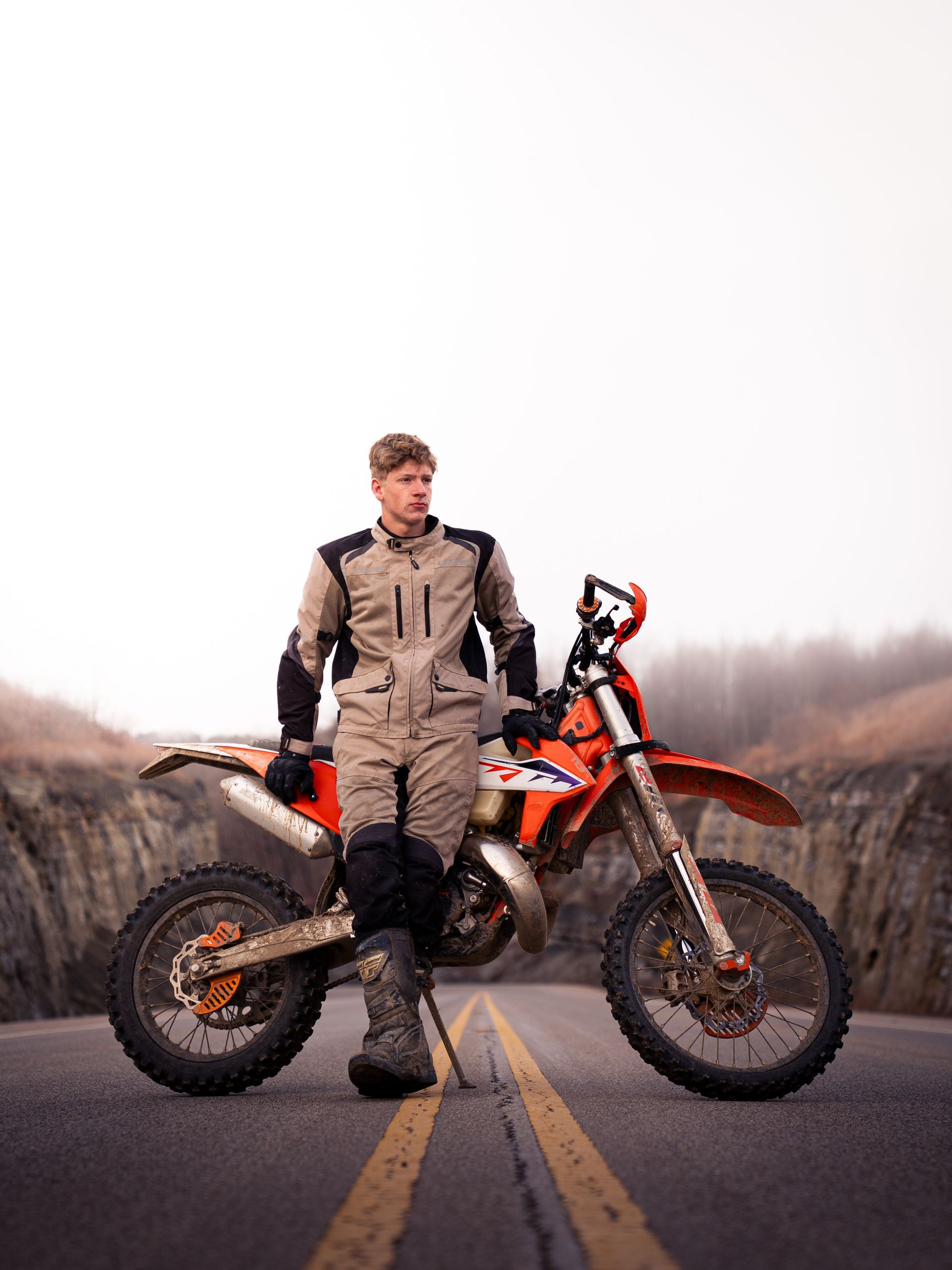 Boy leaning against his dirt bike in the middle of a mountain road for senior photos.