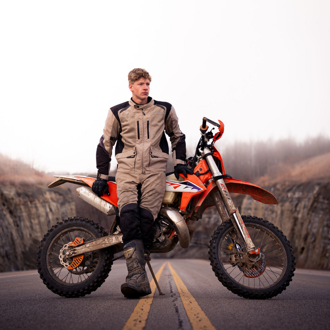 A boy posing for senior photos leaning against a dirt bike on a mountain road.