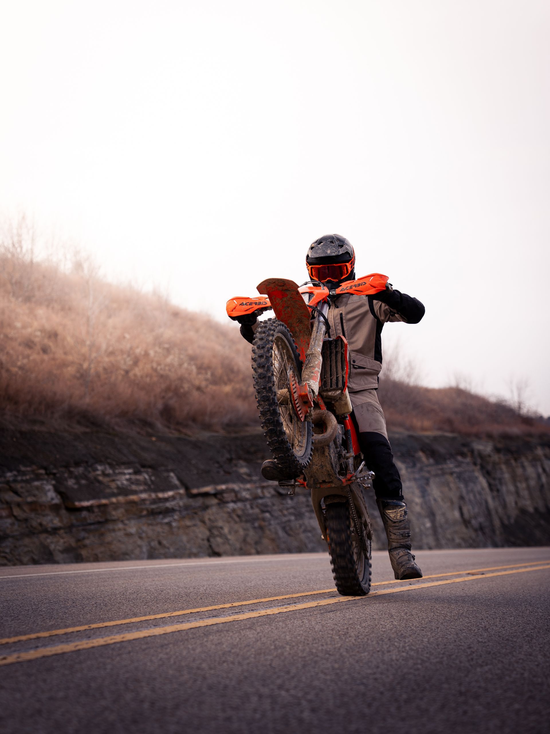 Boy riding a dirt bike down a mountain road doing a wheelie.