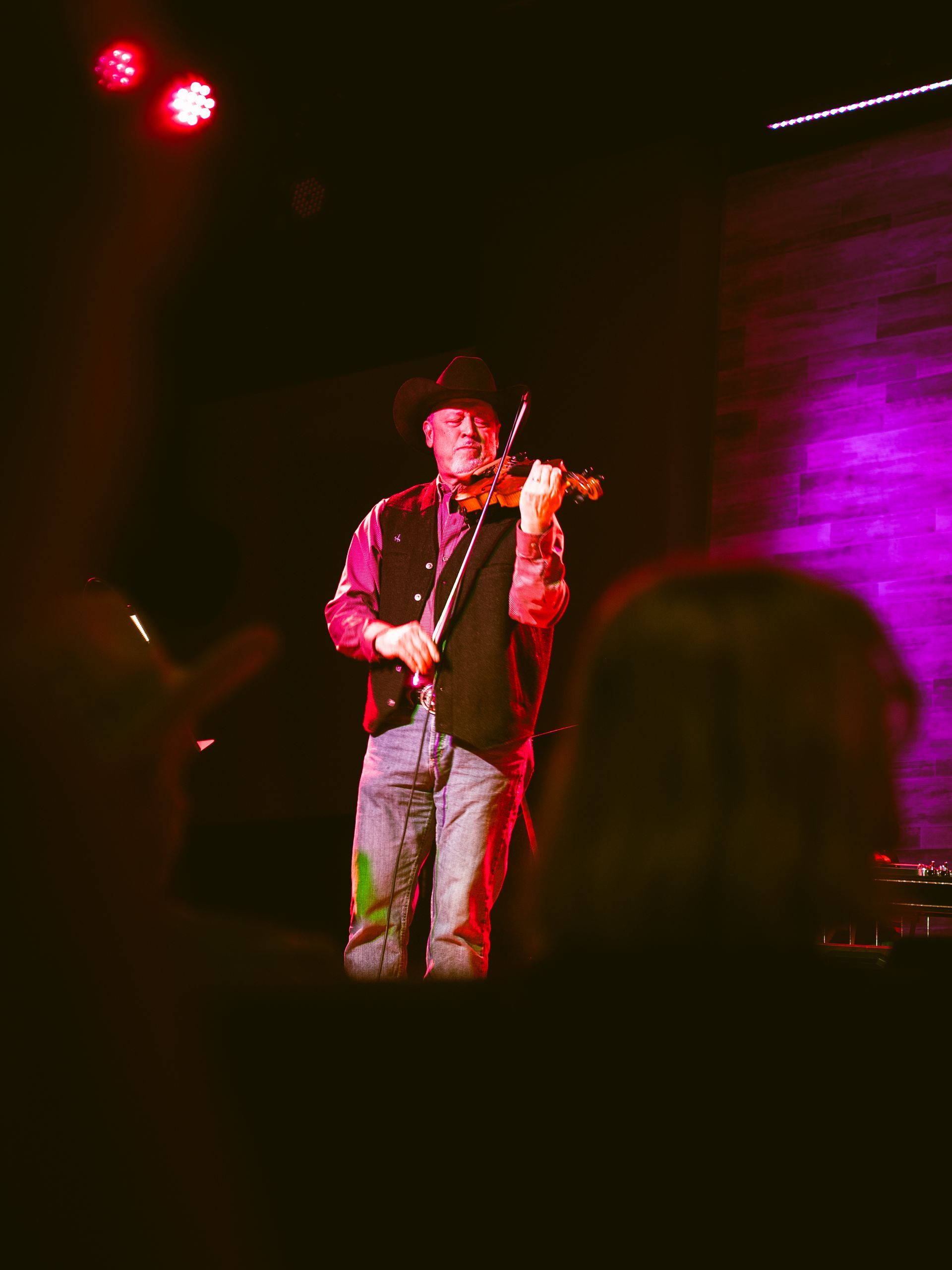 A fiddle player wearing a cowboy hat performs at a live concert.