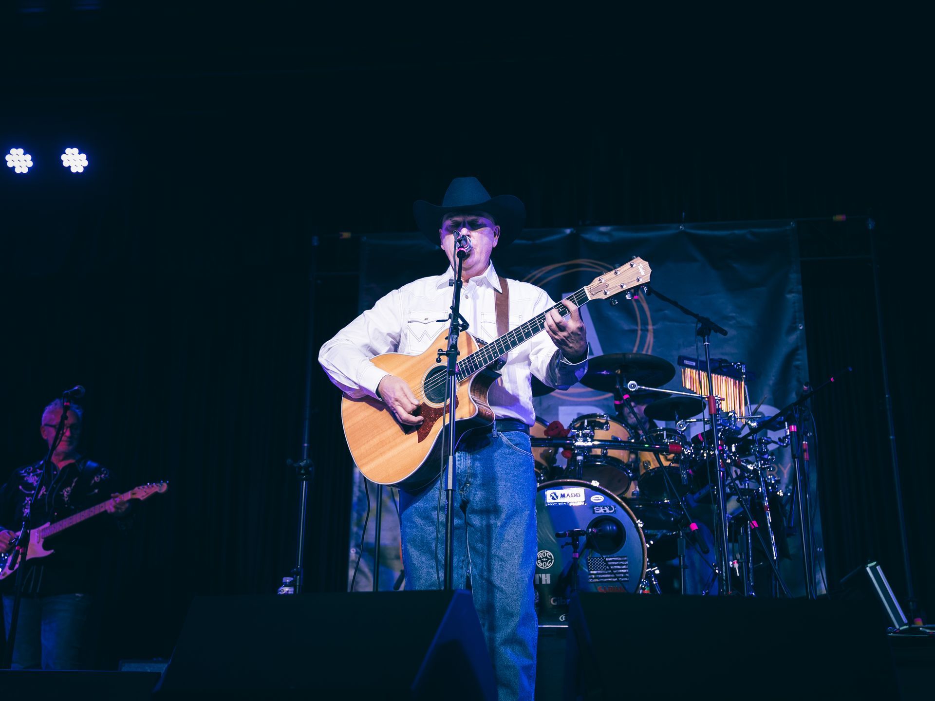 A man stands on stage playing guitar and singing with a full band behind him.