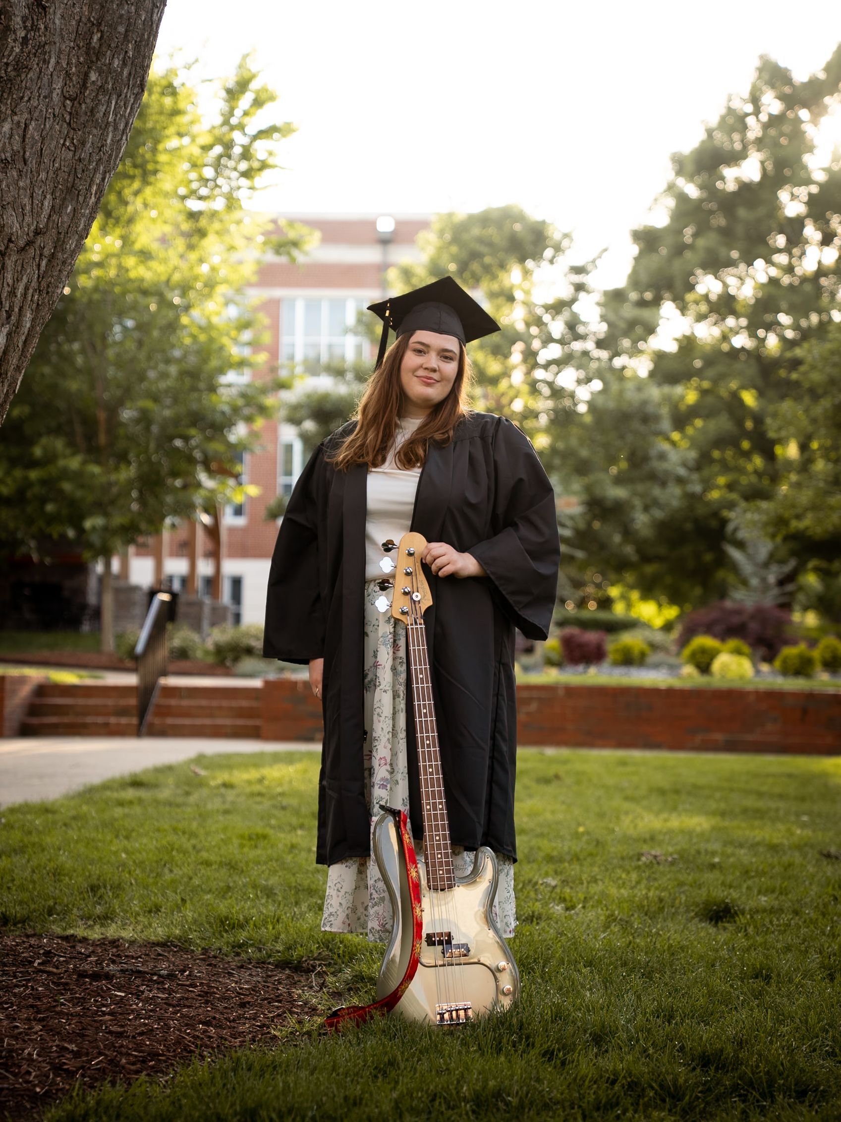 Woman wearing a graduation cap and gown holding a bass guitar.