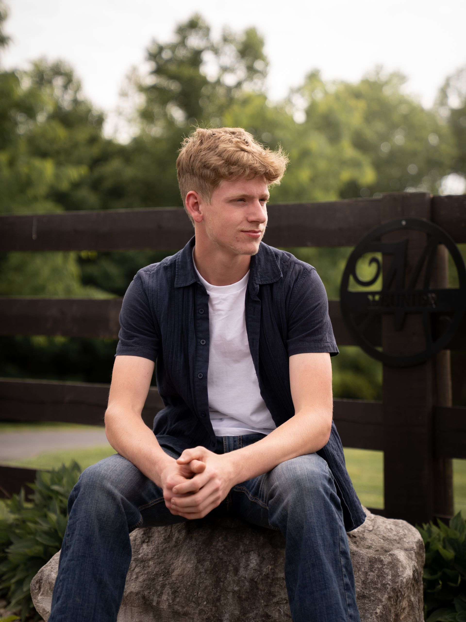 Boy sitting in front of a fence at sunset posing for senior photos.