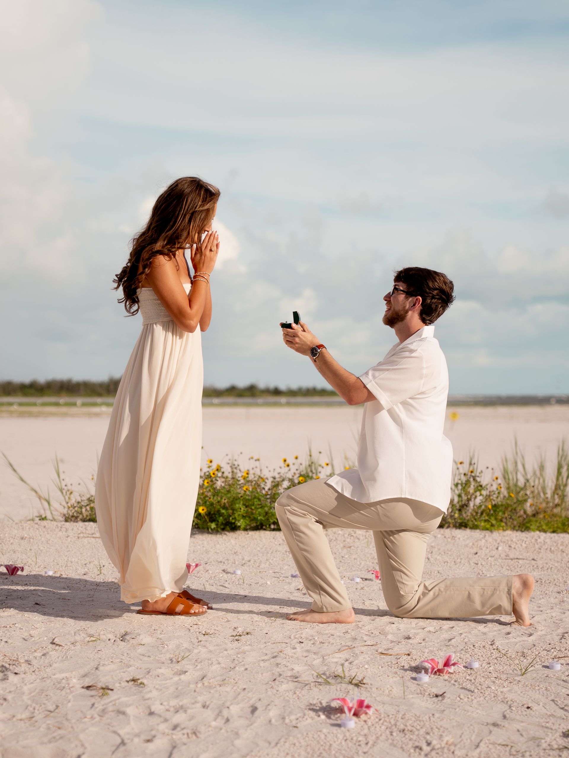 A man is on his knee proposing to his girlfriend on the beach.