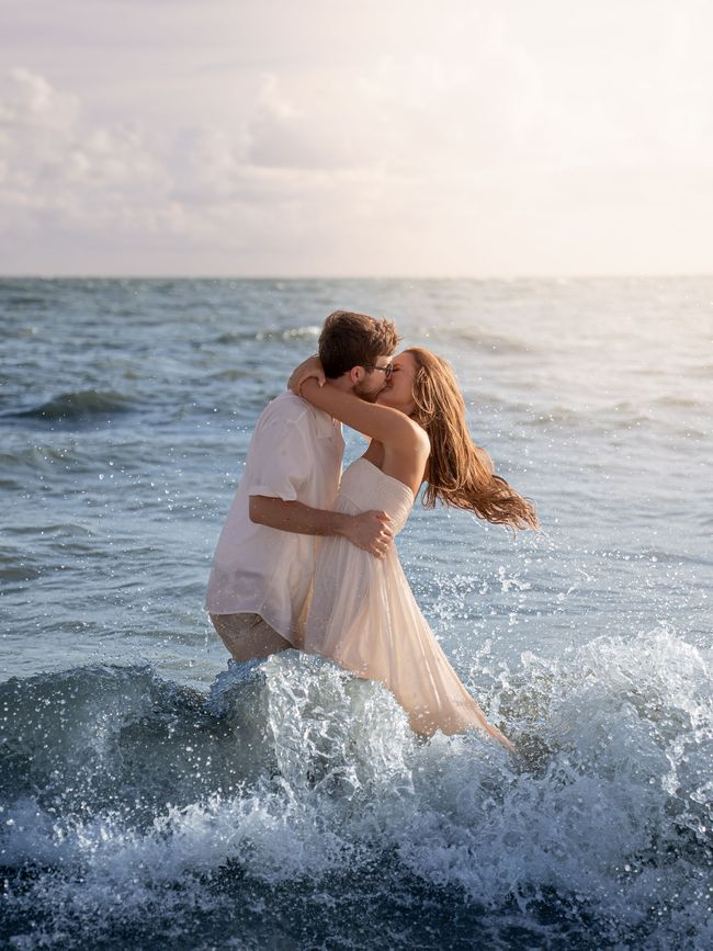 A couple kissing in the ocean as a wave crashes around them