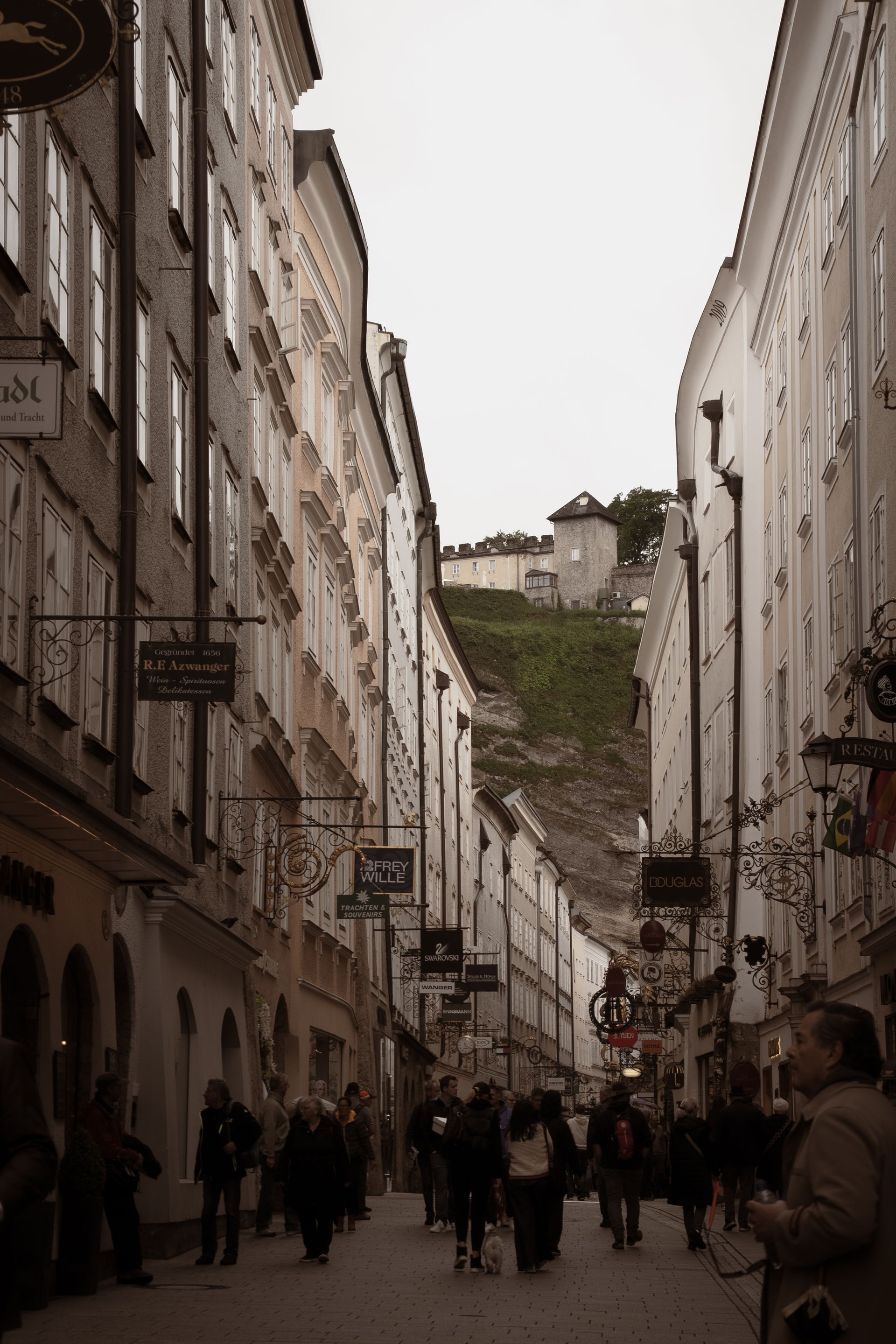 A street in Salzburg, busy with people walking around looking at the stores.