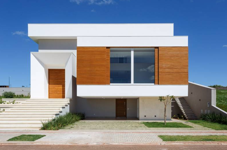 Casa moderna de dois andares, branca e de madeira, com degraus e um fundo de céu azul.